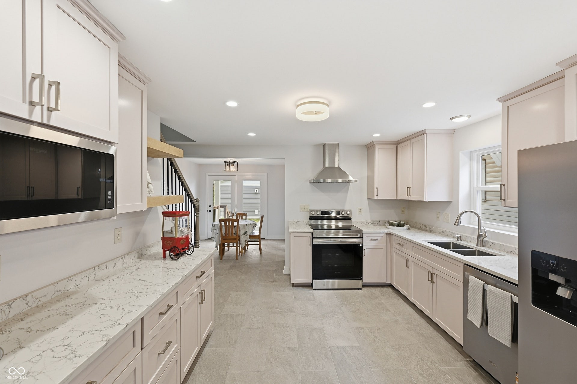 Contemporary kitchen featuring light cabinetry with brushed nickel hardware, white stone countertops, stainless steel appliances, and wood-finish flooring