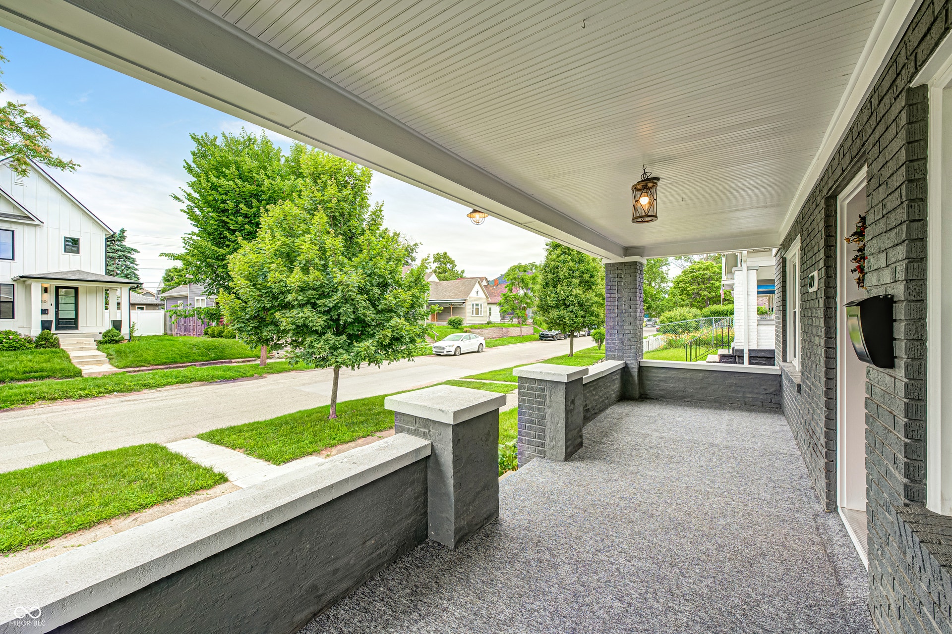 Front porch featuring a gray brick exterior, textured concrete flooring, white beadboard ceiling, suspended lantern-style light fixture, and white trim
