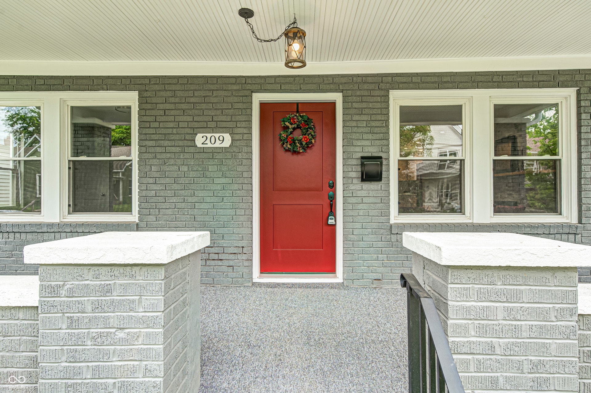 Inviting red entry door with sidelight window, framed by gray brick facade and white window trim