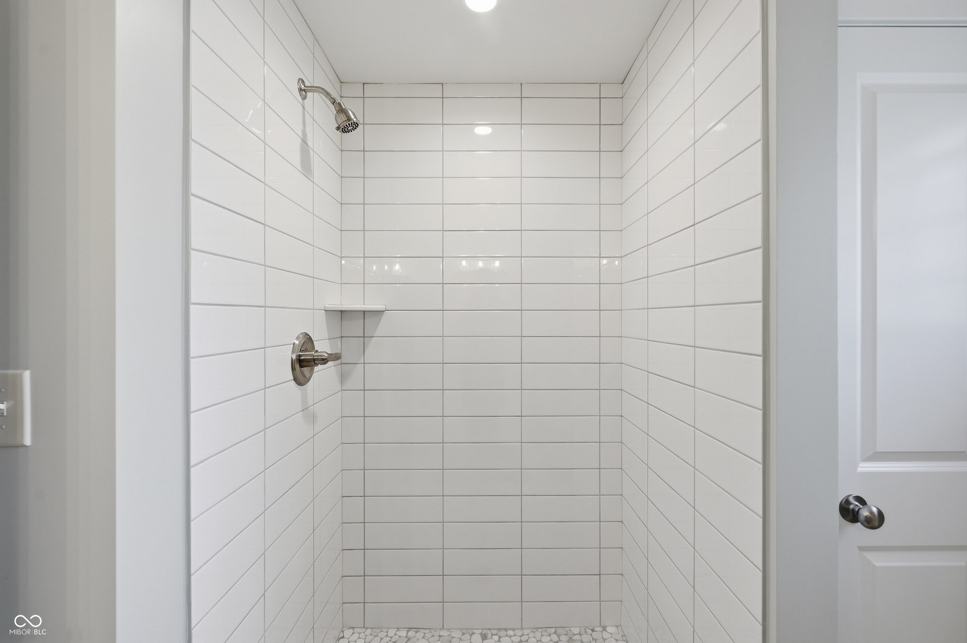 Shower enclosure featuring horizontal subway tile, a built-in shelf, brushed nickel fixtures, a rain showerhead, and a pebble tile floor