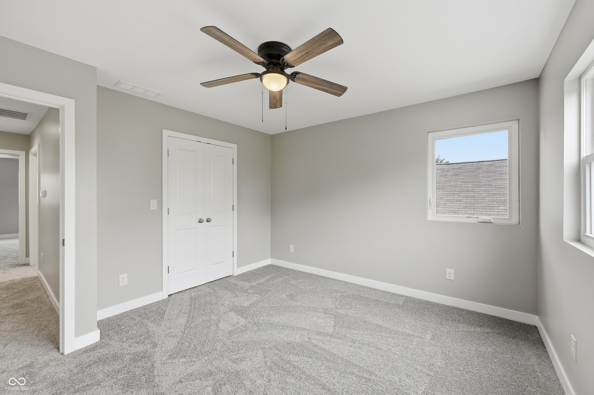 Carpeted room with a ceiling fan, two windows, and a double-door closet