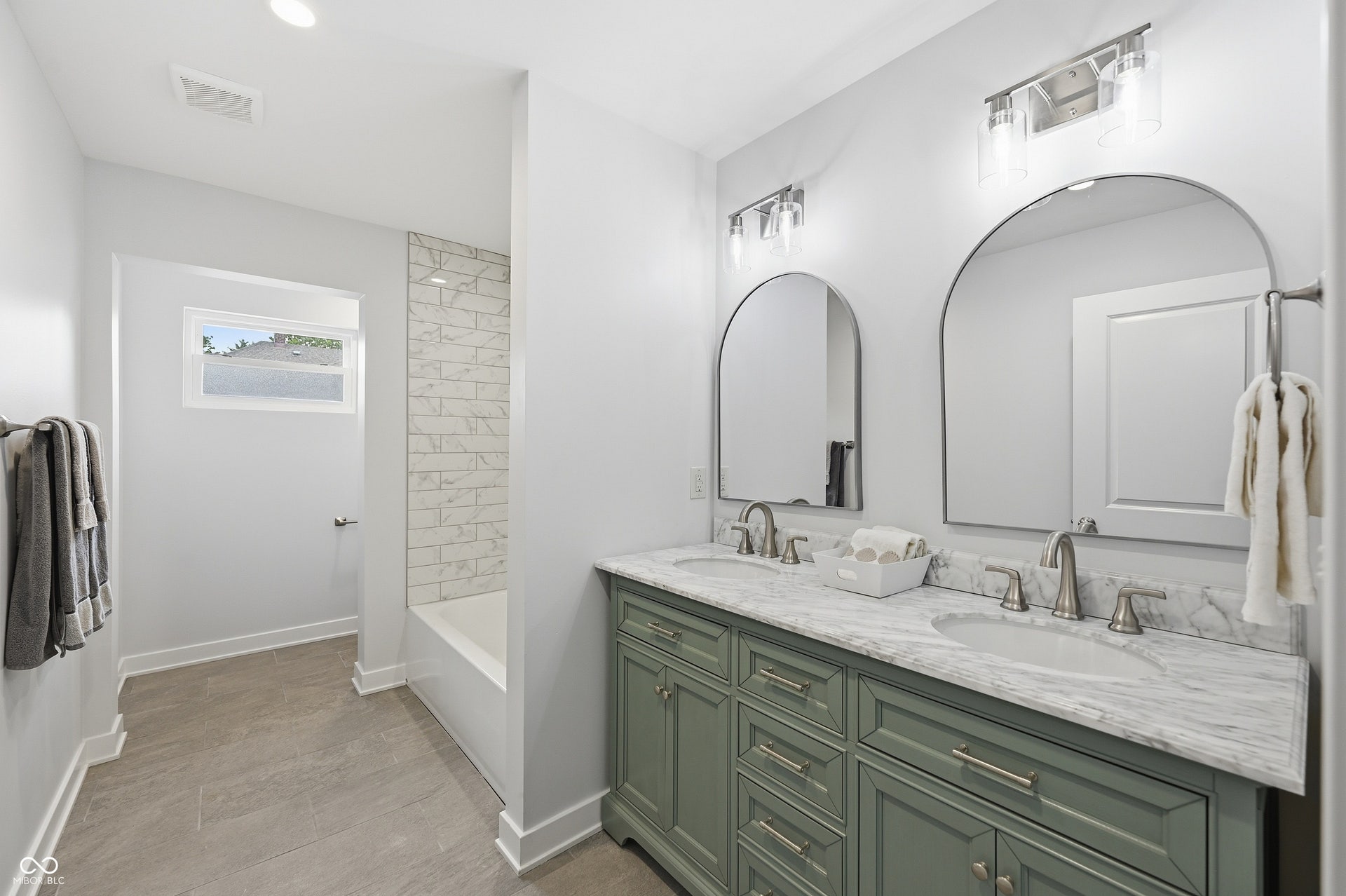Dual arched mirrors above a vanity with two integrated sinks, brushed nickel fixtures, and a marble-patterned countertop