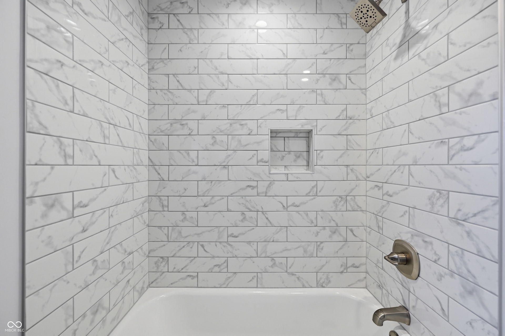 Bathtub shower combination featuring white subway tile surround with gray veining