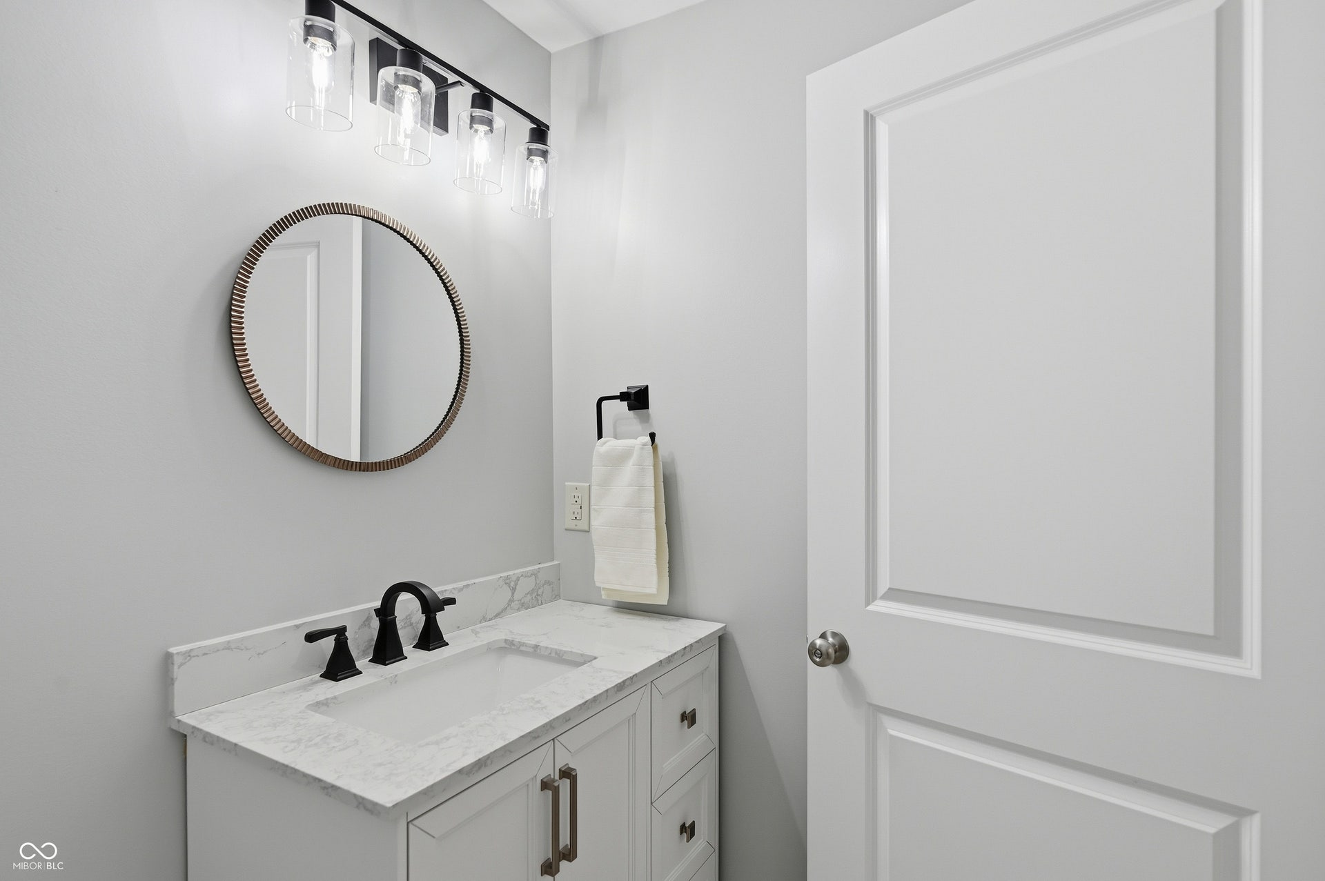 Bathroom vanity featuring a white shaker-style cabinet with drawers and bronze hardware, topped with a stone-finish countertop and integrated rectangular sink