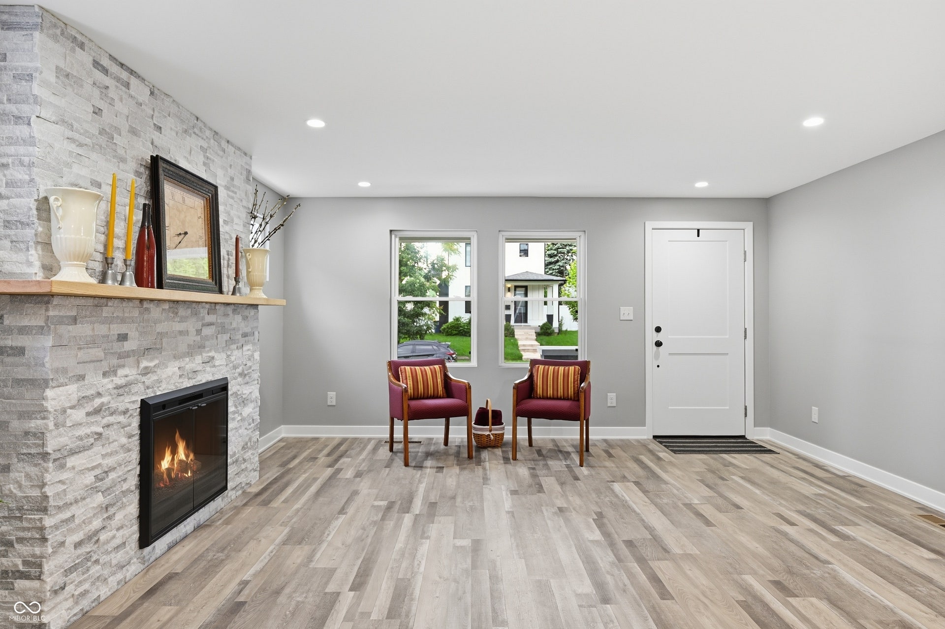 Light-filled living space featuring wood-finish flooring, a stone-clad fireplace with a wood mantel, recessed lighting, and a paneled entry door