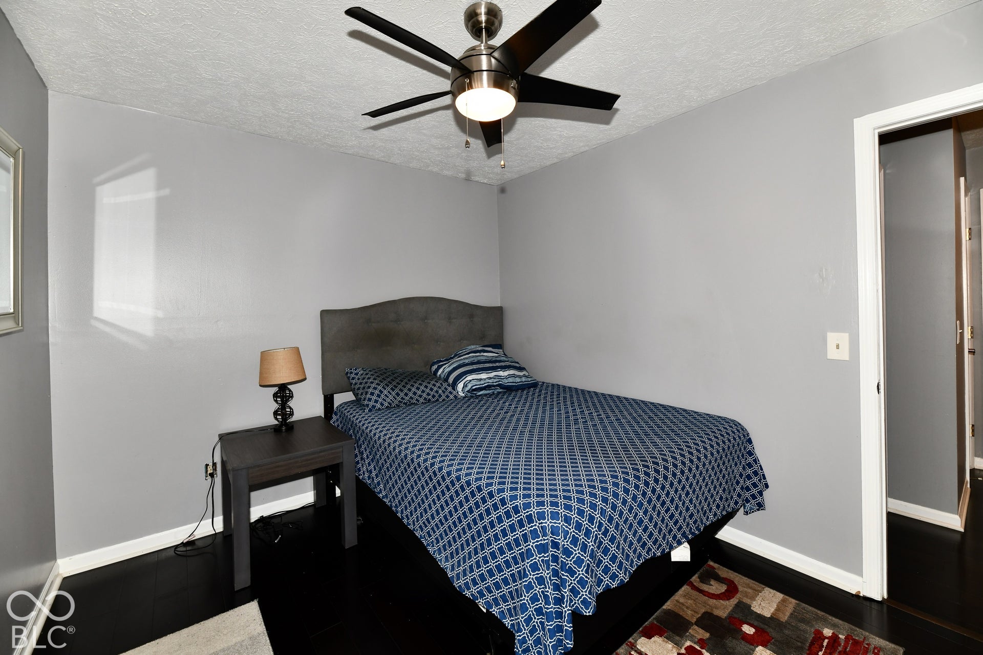 Neutral-toned walls featuring a ceiling-mounted fan with integrated lighting and dark-toned wood-finish flooring