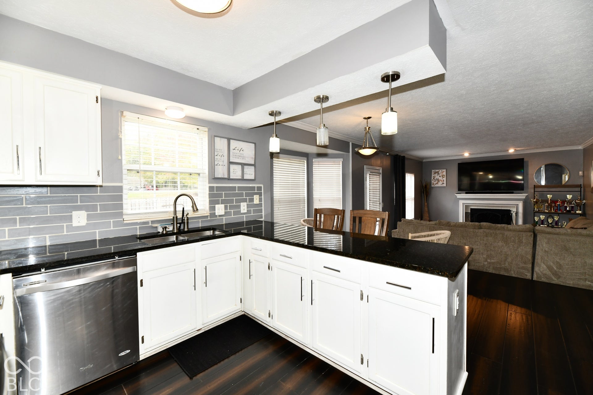 Kitchen featuring white shaker-style cabinetry, dark stone countertops, stainless steel dishwasher, subway tile backsplash, and three glass pendant lights