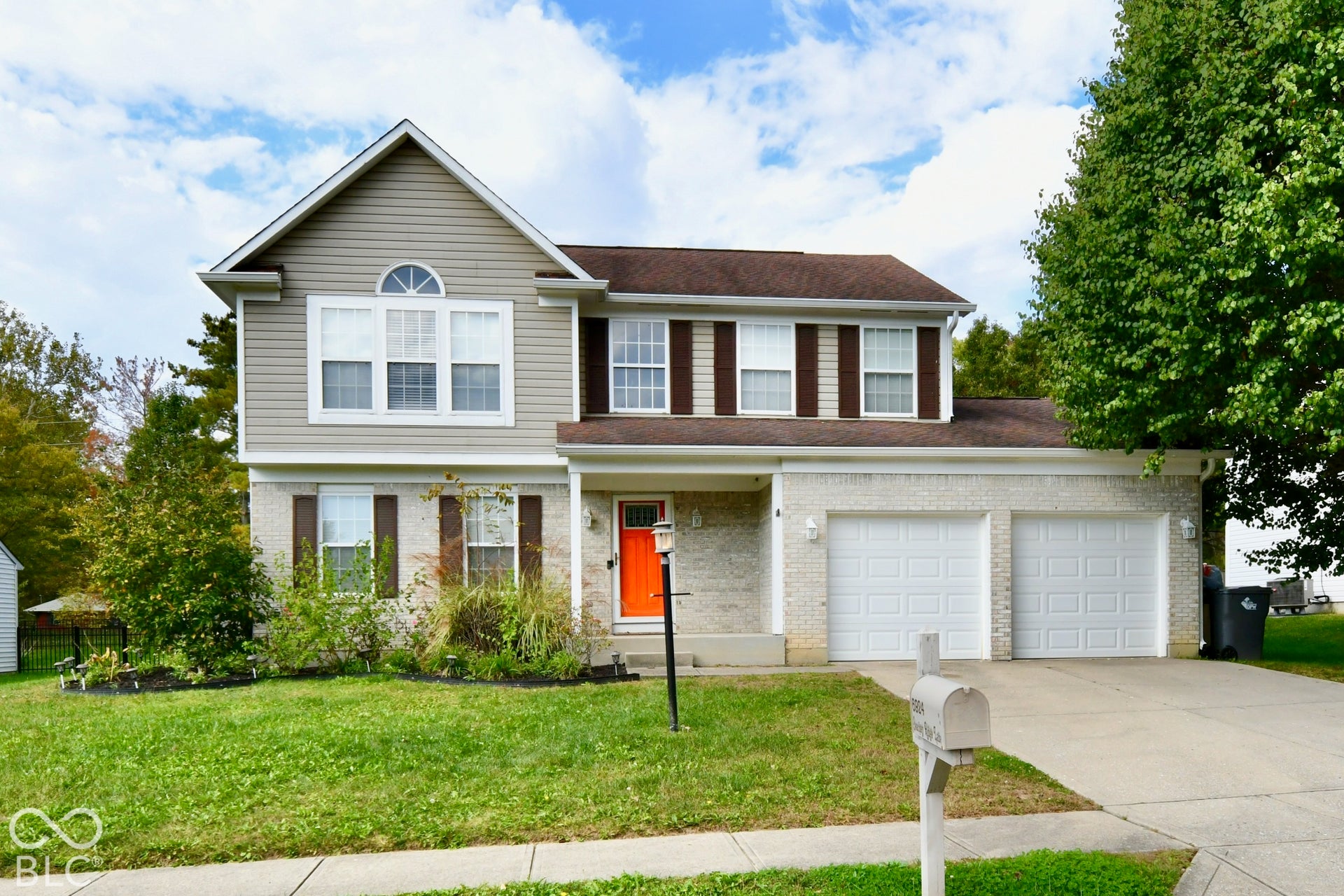 Two-story residence featuring light-colored brick and horizontal siding, an attached two-car garage, decorative window shutters, and a covered front entryway