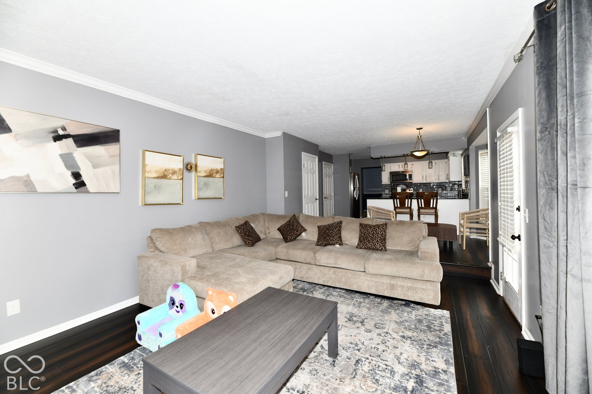 Open-concept living space featuring wood-finish flooring, crown molding, a kitchen peninsula with bar-style seating, and recessed lighting