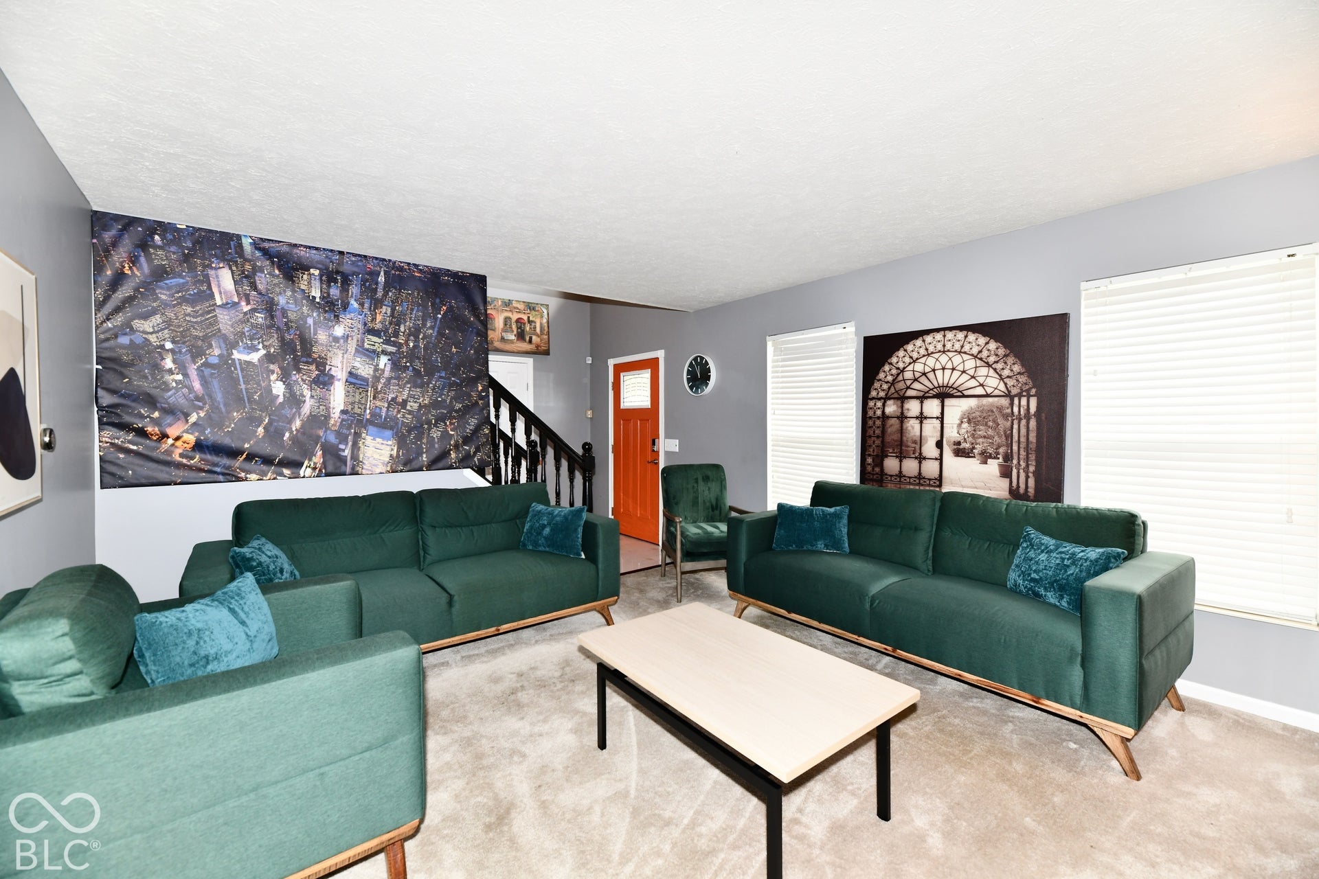 Living area featuring neutral carpeting, grey wall paint, horizontal window blinds, and a staircase with a dark wood banister