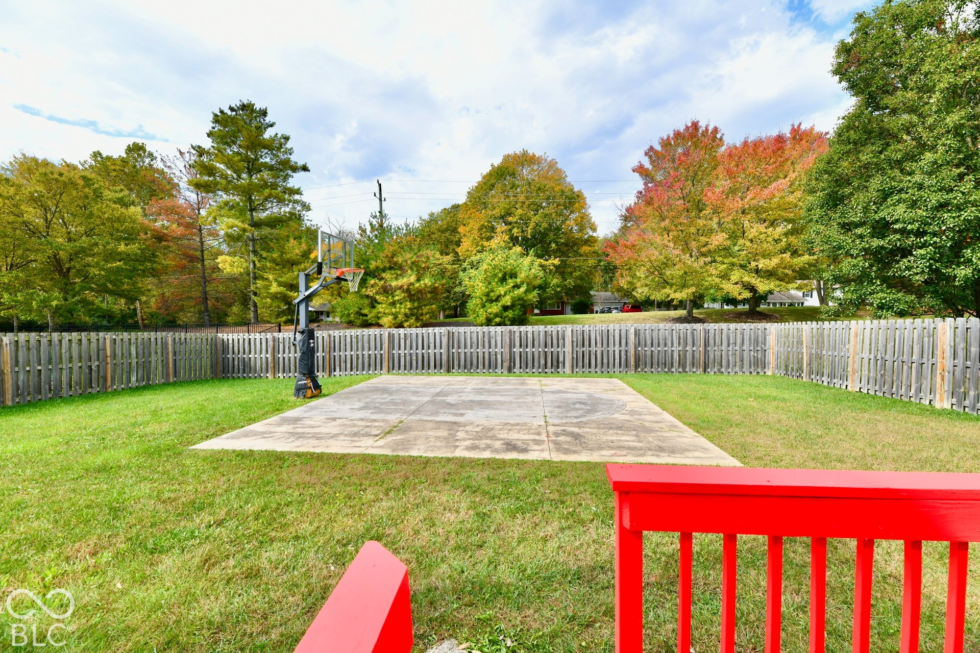 Backyard featuring a concrete sport court, built-in basketball hoop, perimeter wood privacy fencing, and expansive grass lawn