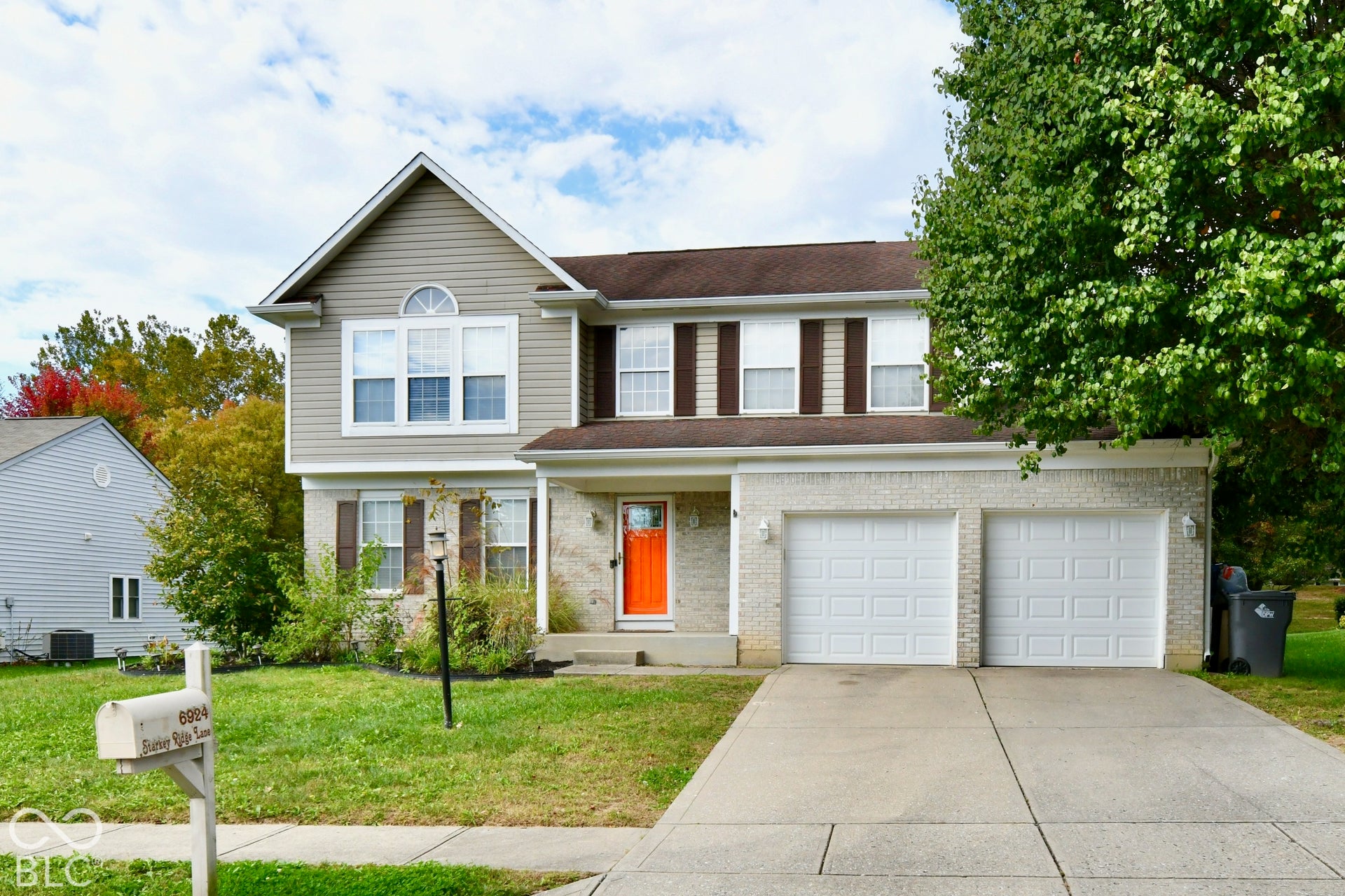 Two-story residence featuring a mixed-material facade of light-toned brick and horizontal siding, an attached two-car garage, and a covered front entryway