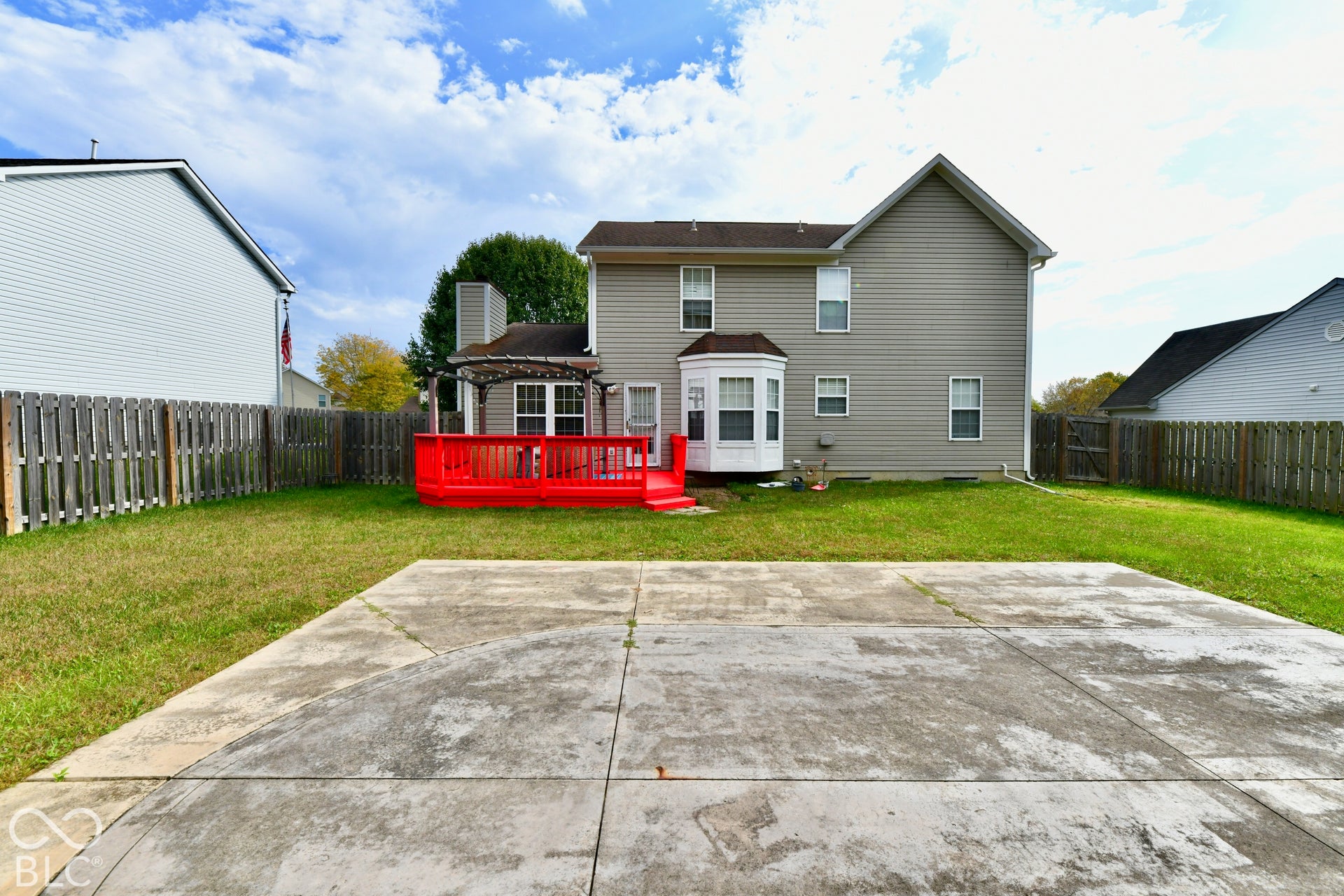 Rear exterior featuring a tiered wooden deck with an integrated pergola, concrete patio, bay window, and fenced backyard