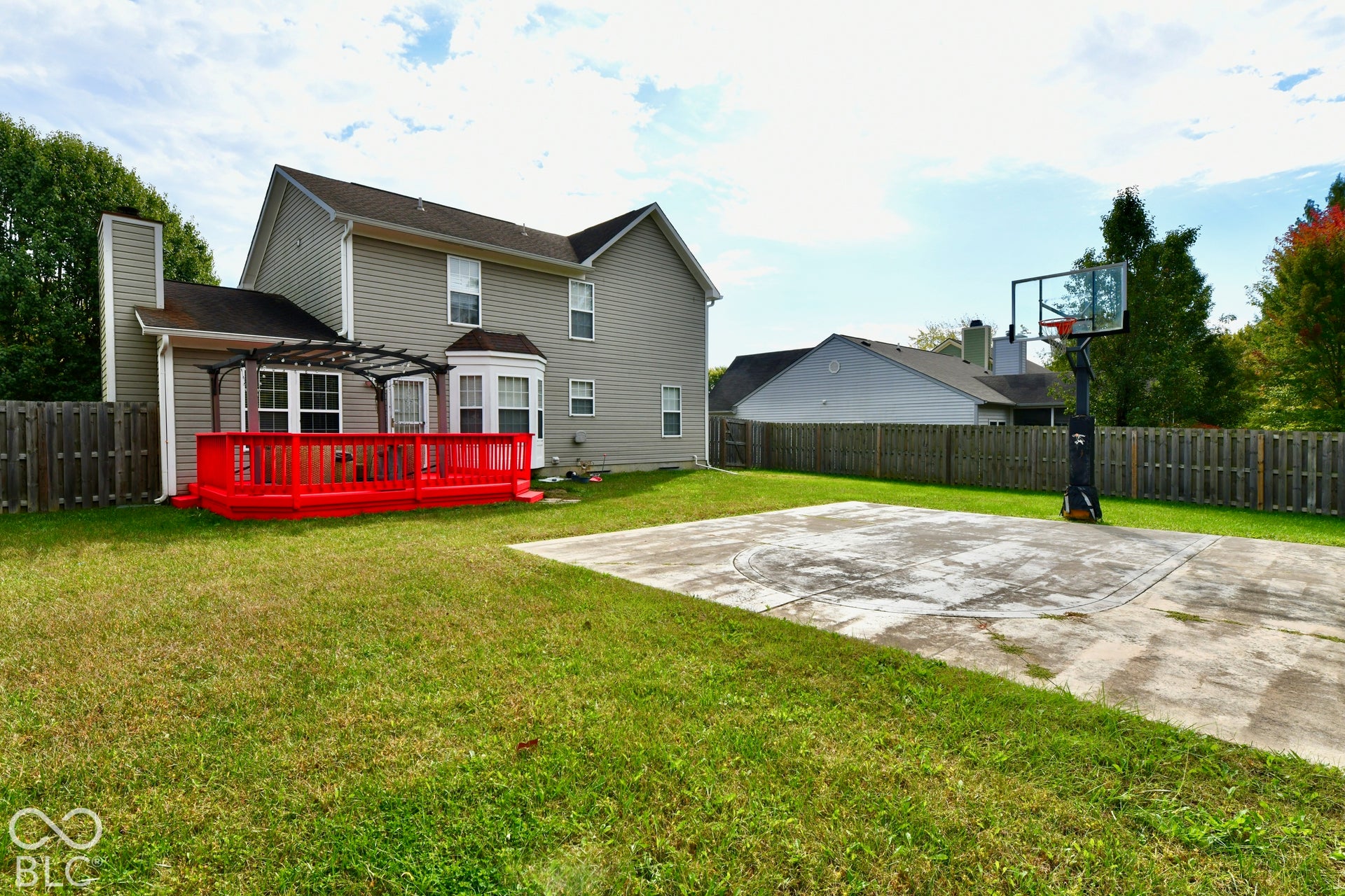 Backyard featuring a wood deck with a pergola, a concrete sports court, and perimeter wood privacy fencing