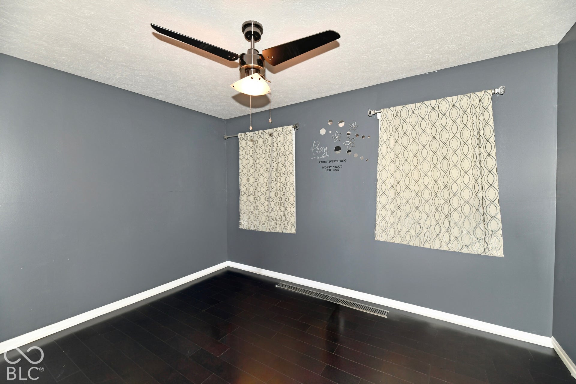 Room featuring wood-finish flooring, charcoal-toned walls, and a ceiling-mounted light fixture with a fan