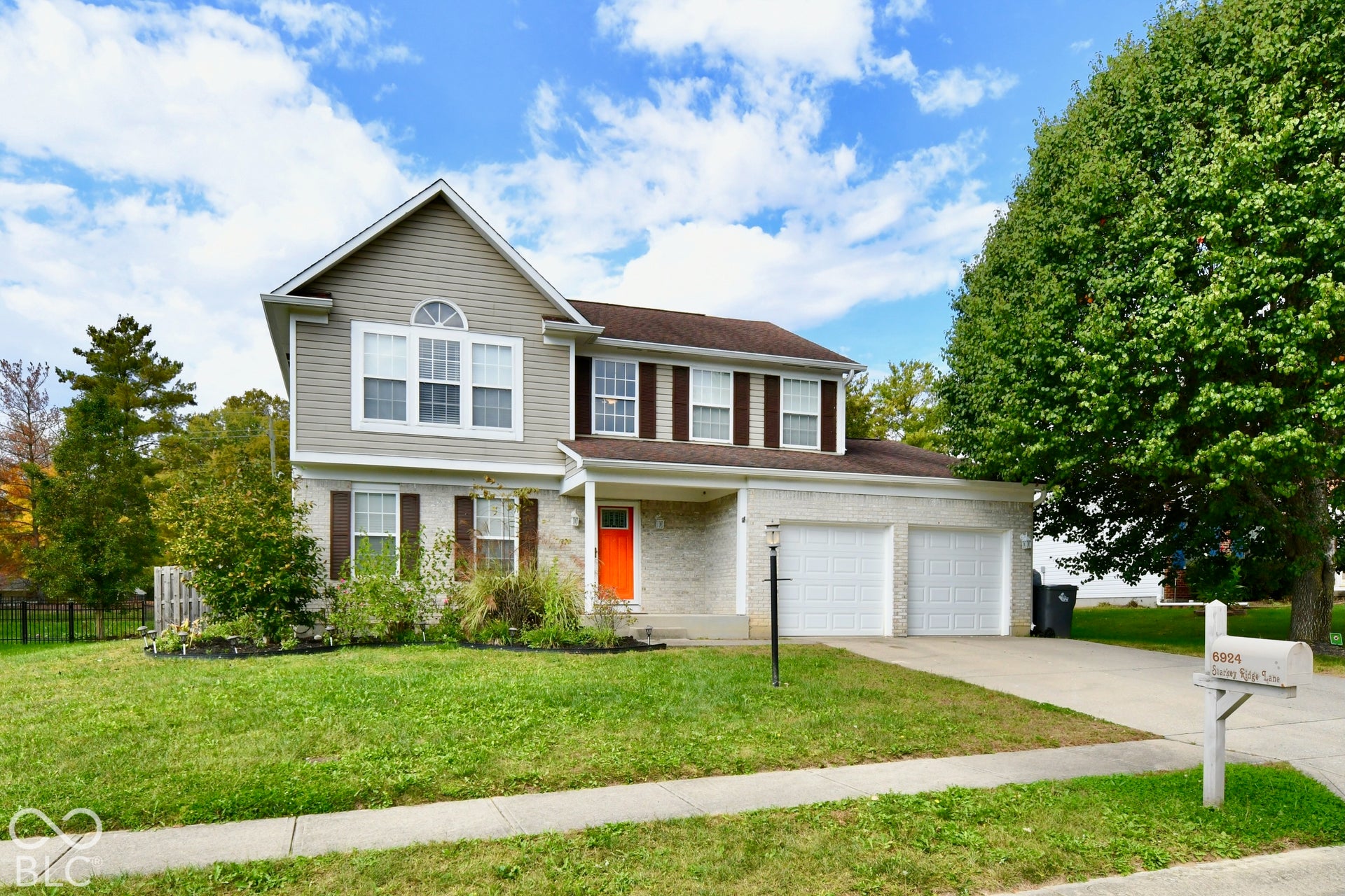 Two-story exterior featuring a brick and horizontal siding facade, a covered front porch, a two-car garage, and multiple paneled windows with shutters