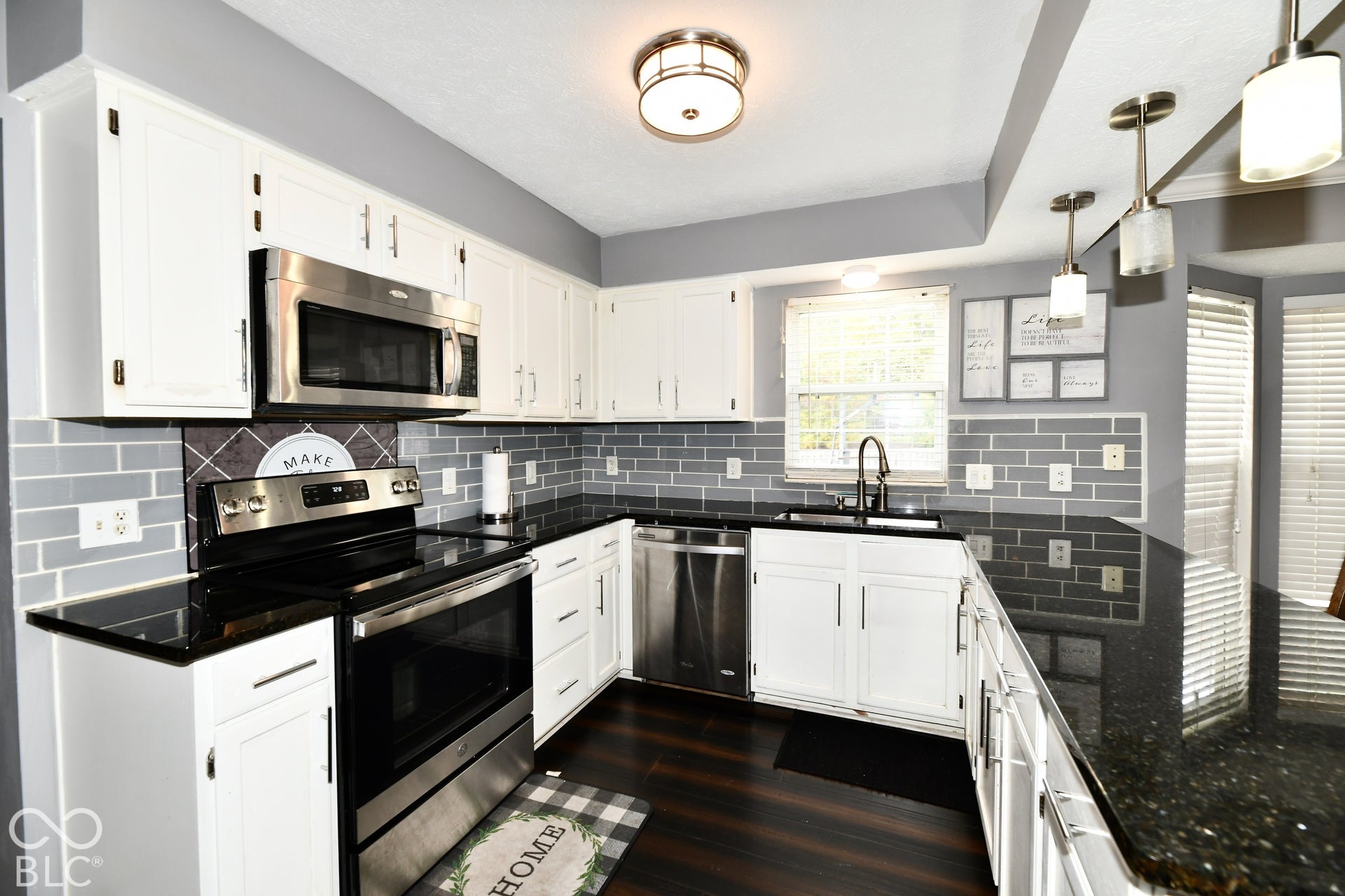 Kitchen featuring white shaker-style cabinetry, dark stone countertops, stainless steel appliances, grey subway tile backsplash, and dark wood-finish flooring
