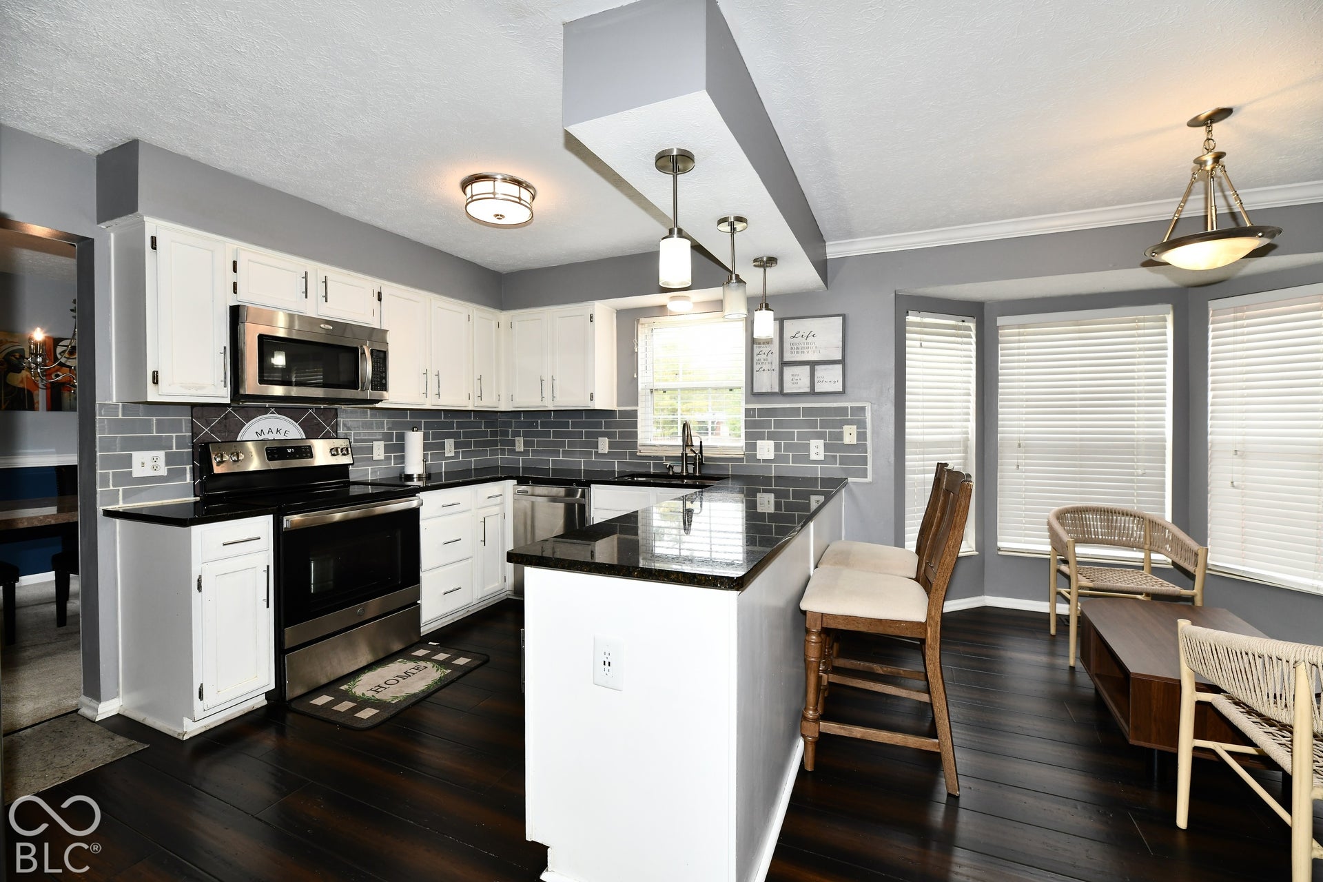 Kitchen featuring white cabinetry, dark countertops, brick-patterned tile backsplash, pendant lighting over a breakfast bar, and wood-finish flooring