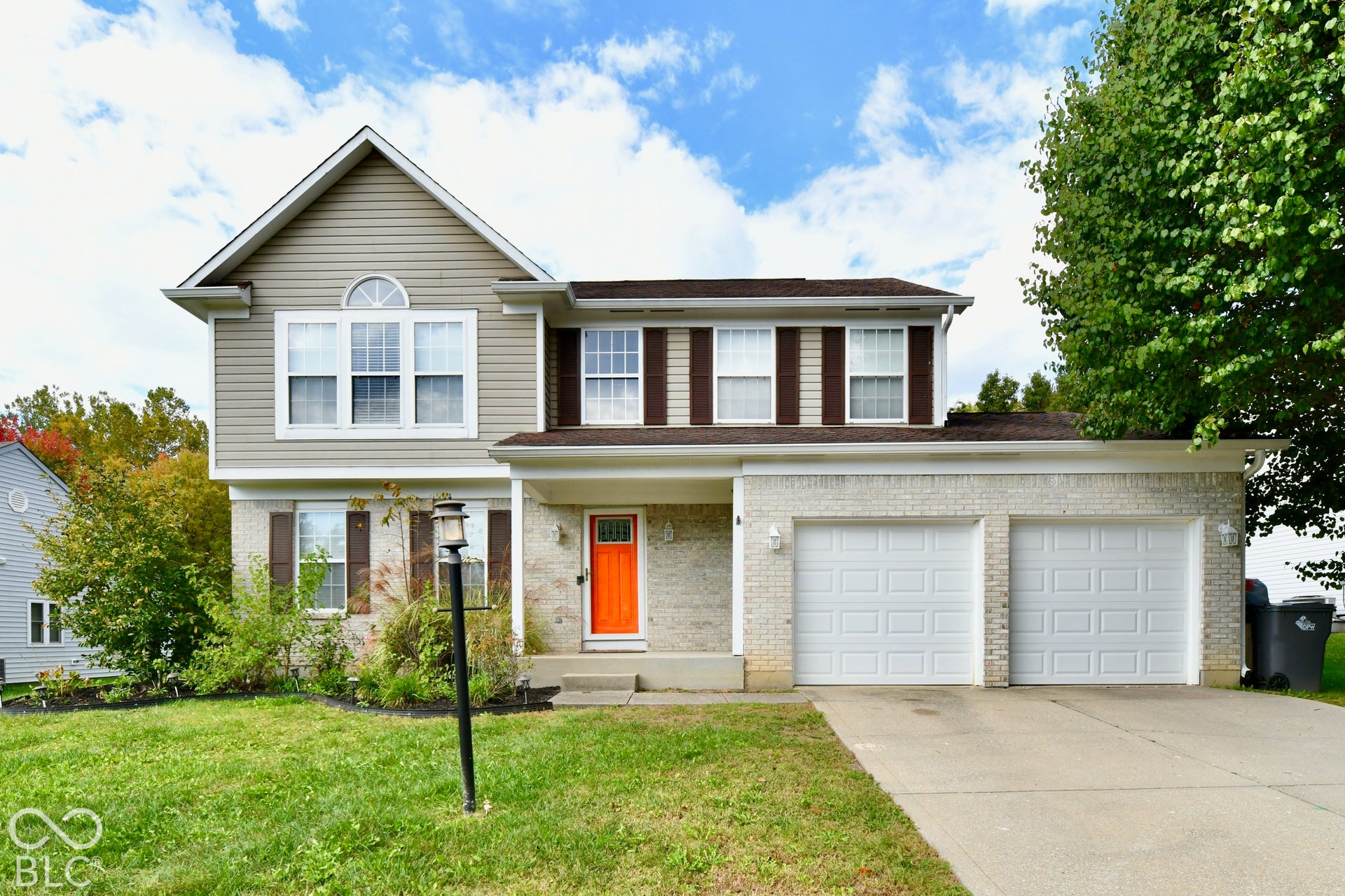 Two-story exterior featuring light-colored brick and horizontal siding, an attached two-car garage, shuttered windows, a decorative arched transom, and a concrete driveway