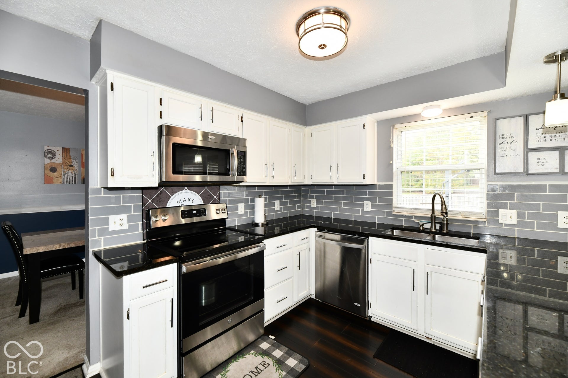 Kitchen featuring white cabinetry, dark stone-finish countertops, stainless steel appliances, grey subway tile backsplash, and wood-finish flooring