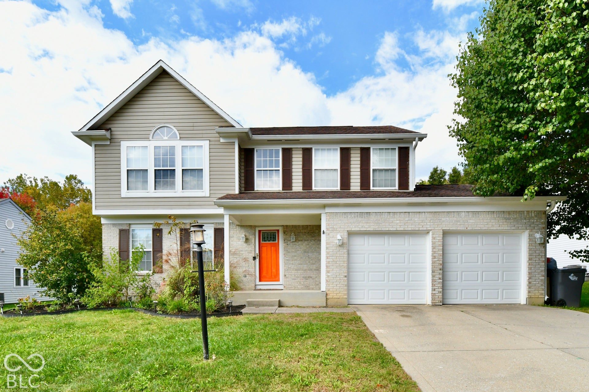 Two-story exterior featuring light-toned masonry, neutral vinyl siding, an attached two-car garage, and decorative shutters