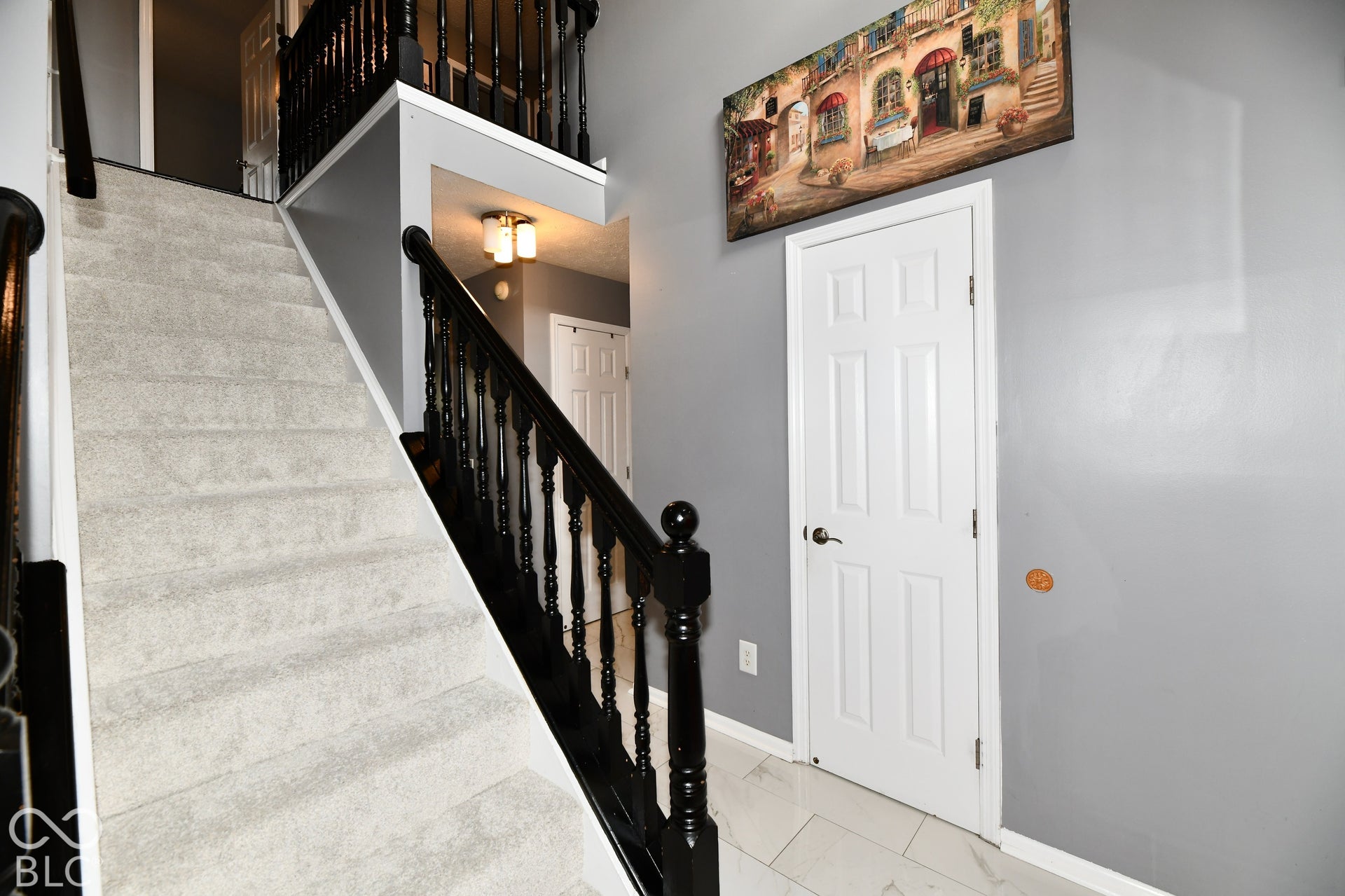Foyer featuring white tile flooring, a staircase with carpeted treads, and a black-painted wood balustrade