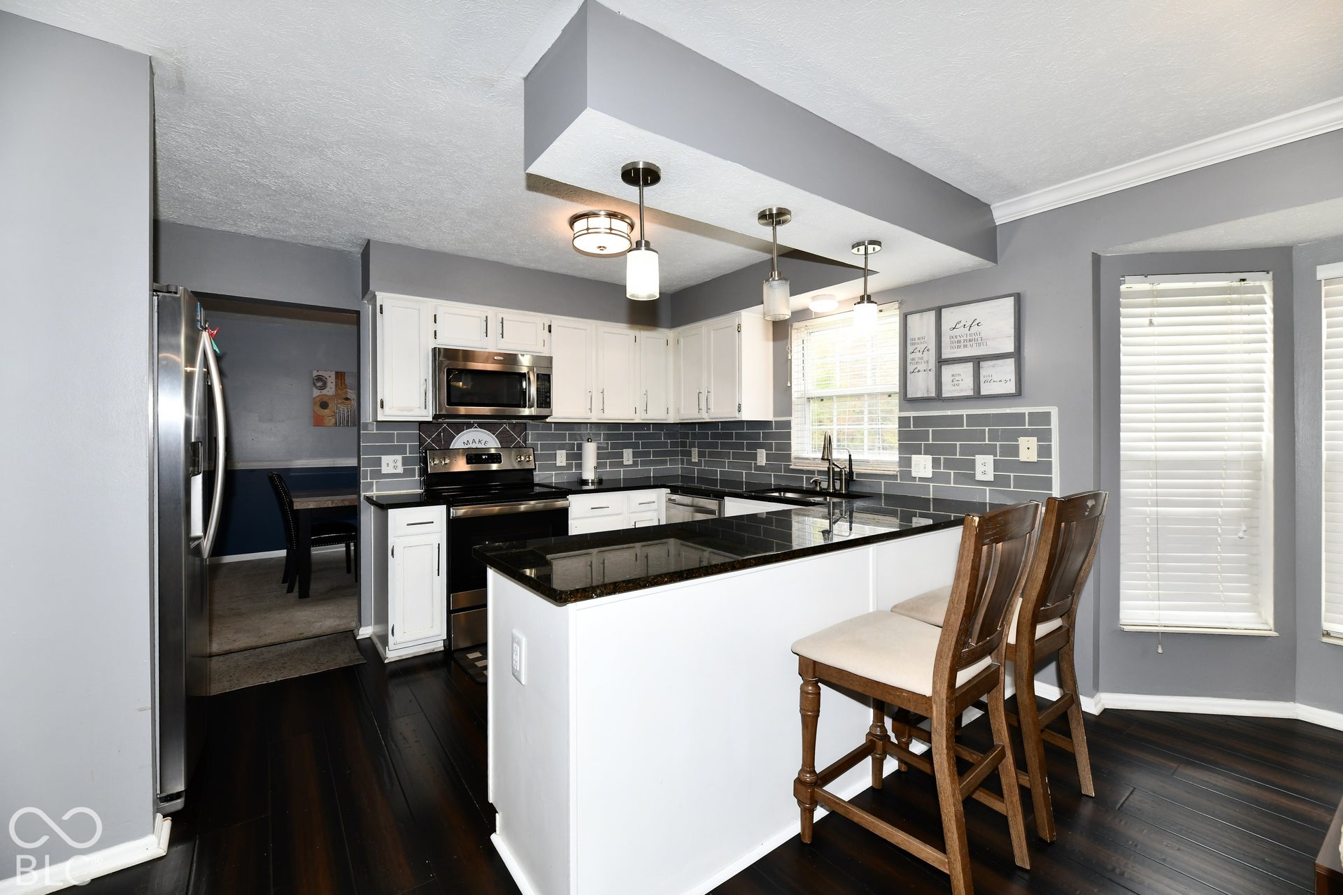Kitchen featuring white shaker-style cabinetry, dark stone-finish countertops, subway tile backsplash, stainless steel appliances, and dark wood-finish flooring