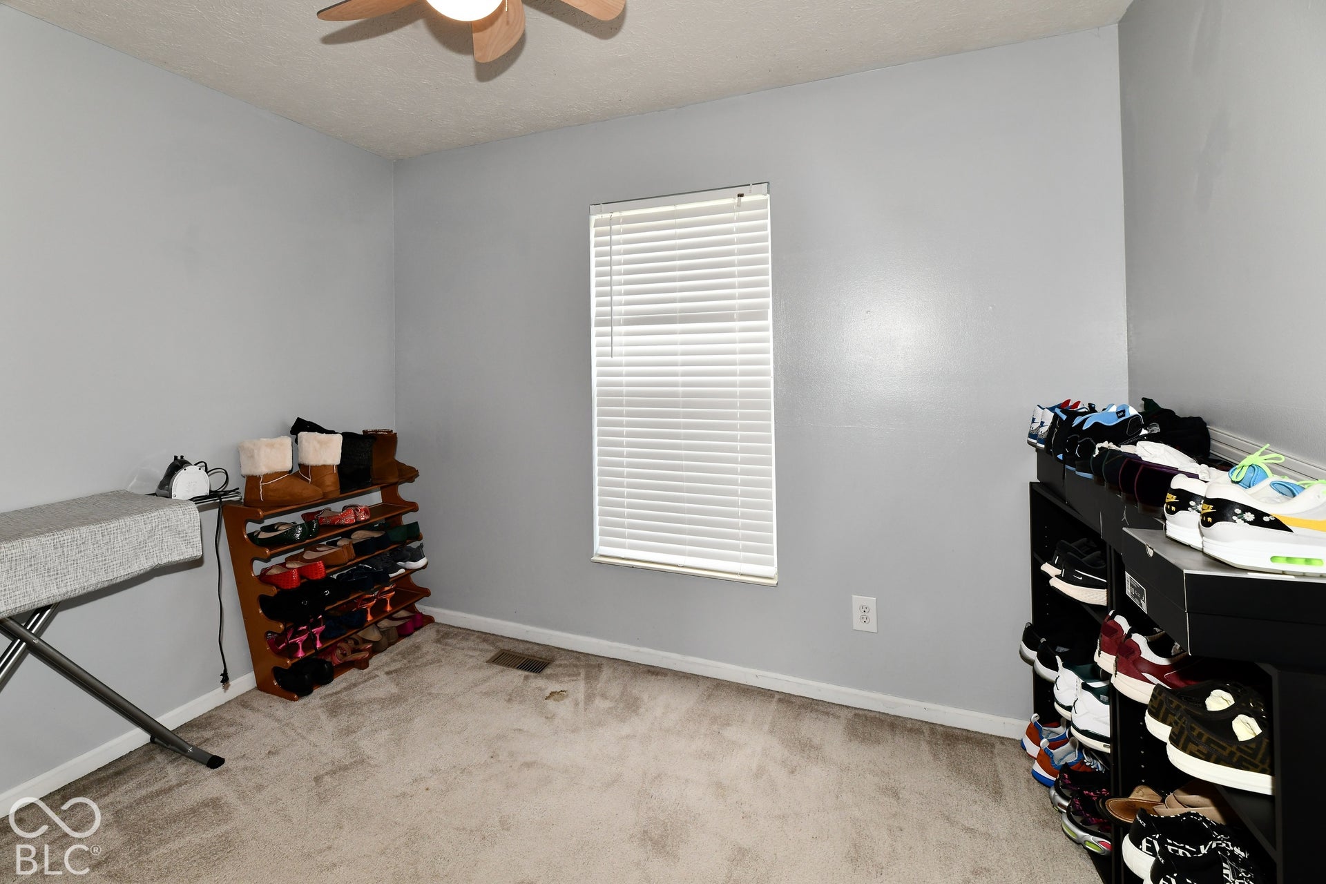 Neutral-toned interior room featuring wall-to-wall carpeting, a single window with horizontal blinds, and a ceiling-mounted light fixture