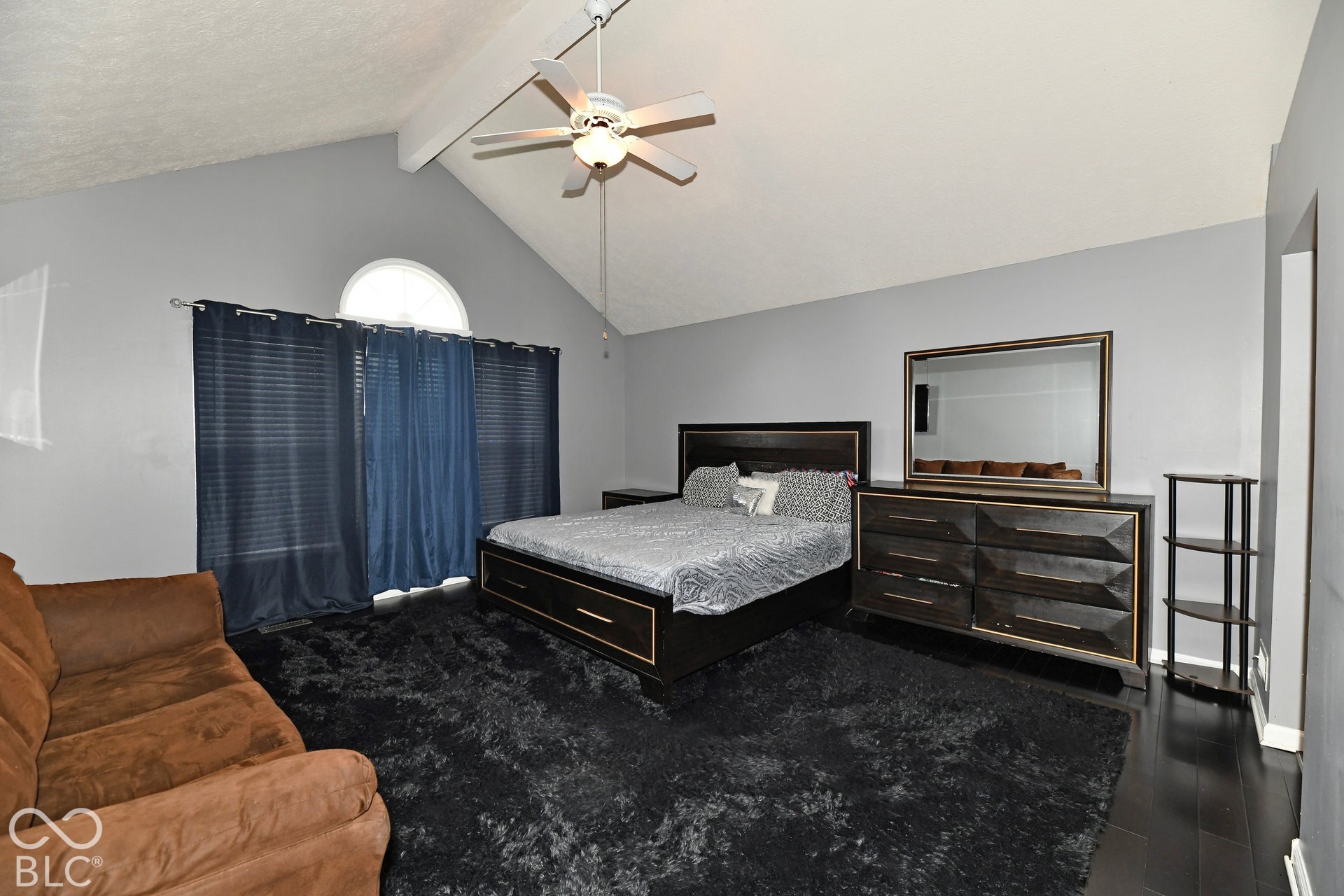 Vaulted ceilings featuring a central support beam, arched accent window, and a ceiling-mounted light fixture with fan