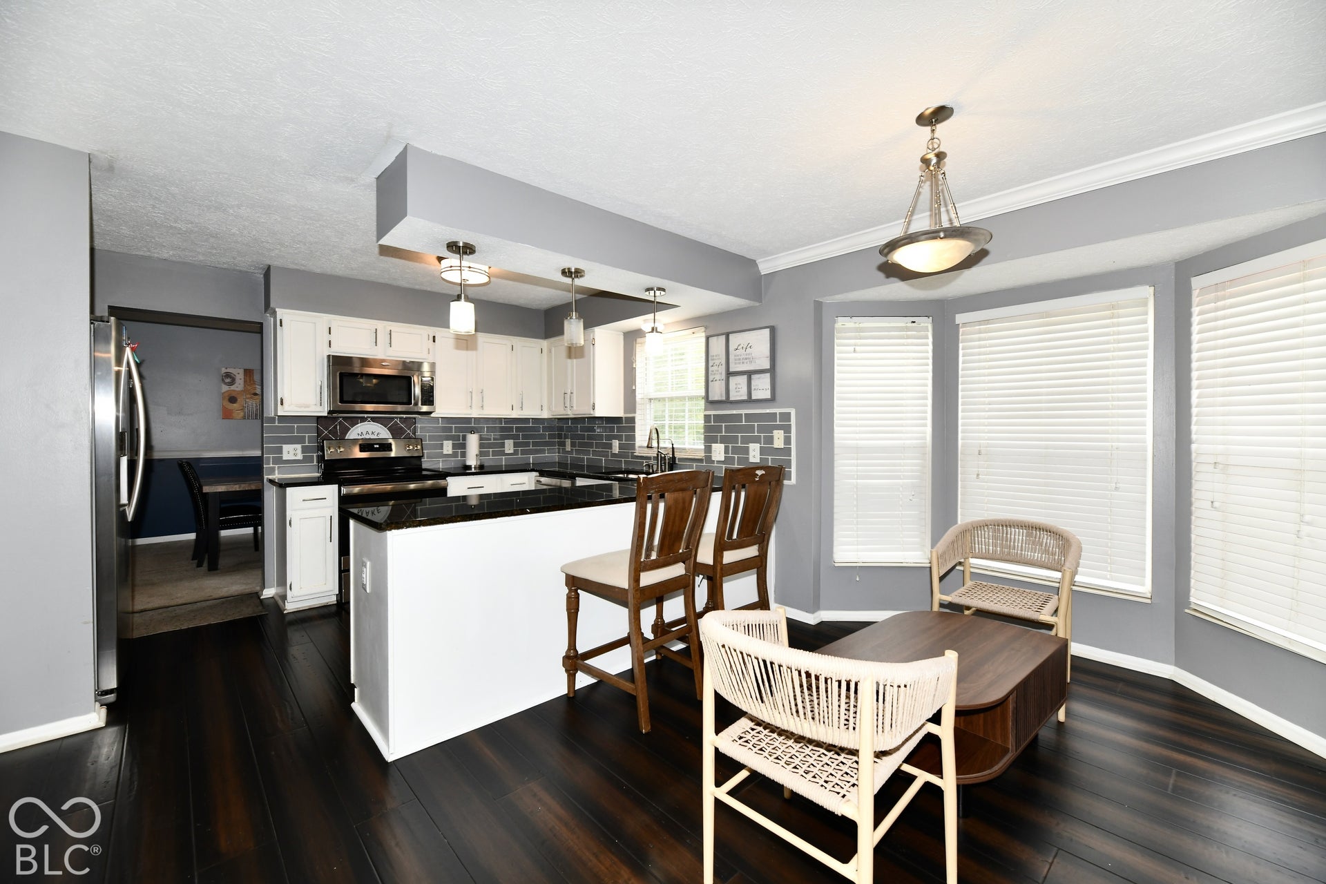 Kitchen featuring dark stone countertops, white cabinetry, subway tile backsplash, wood-finish flooring, and a multi-window bay area
