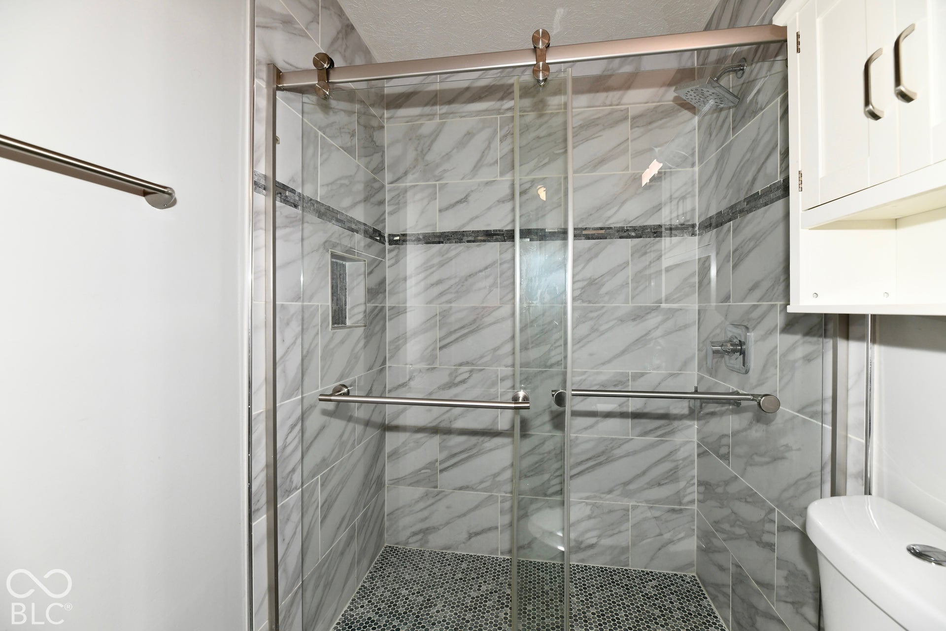 Walk-in shower featuring glass sliding doors, stone-patterned wall tile, a recessed storage niche, pebble-style floor tile, and a wall-mounted medicine cabinet