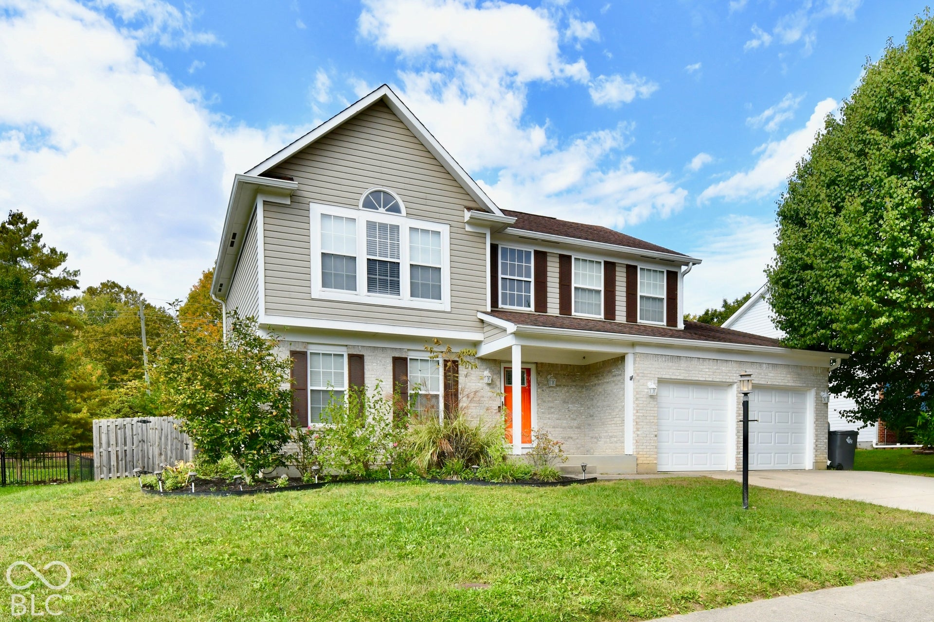 Two-story exterior featuring a brick and horizontal siding facade, a covered front porch, an attached two-car garage, and a decorative arched window