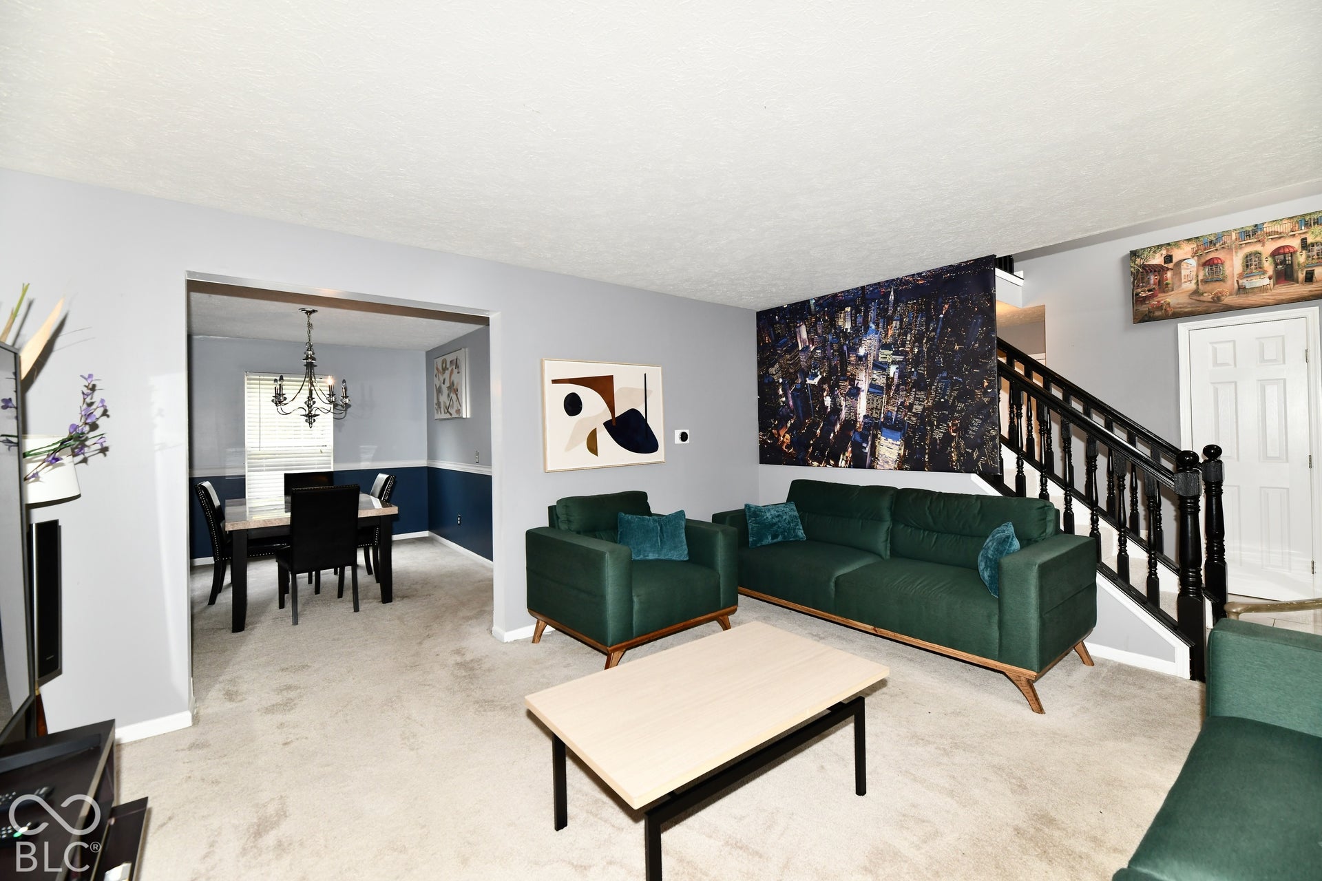Interior space featuring neutral-toned carpeting, staircase with dark-finished wooden balusters, and a chair rail in the dining area
