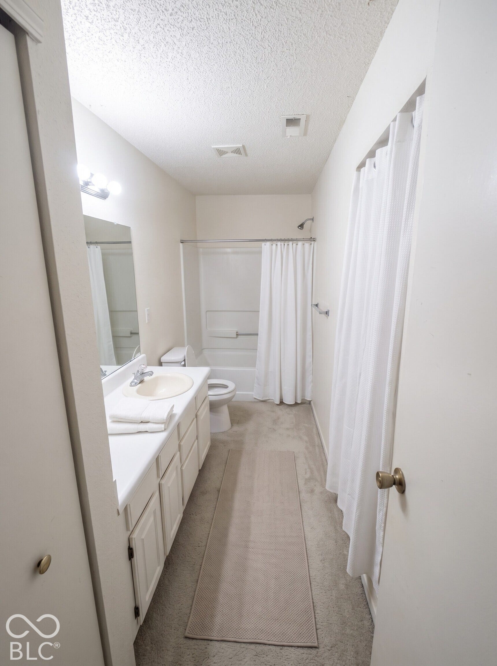 Virtually Altered - Bathroom featuring white cabinetry, integrated sink, vanity mirror with light fixture, and a tub-shower combination with enclosure