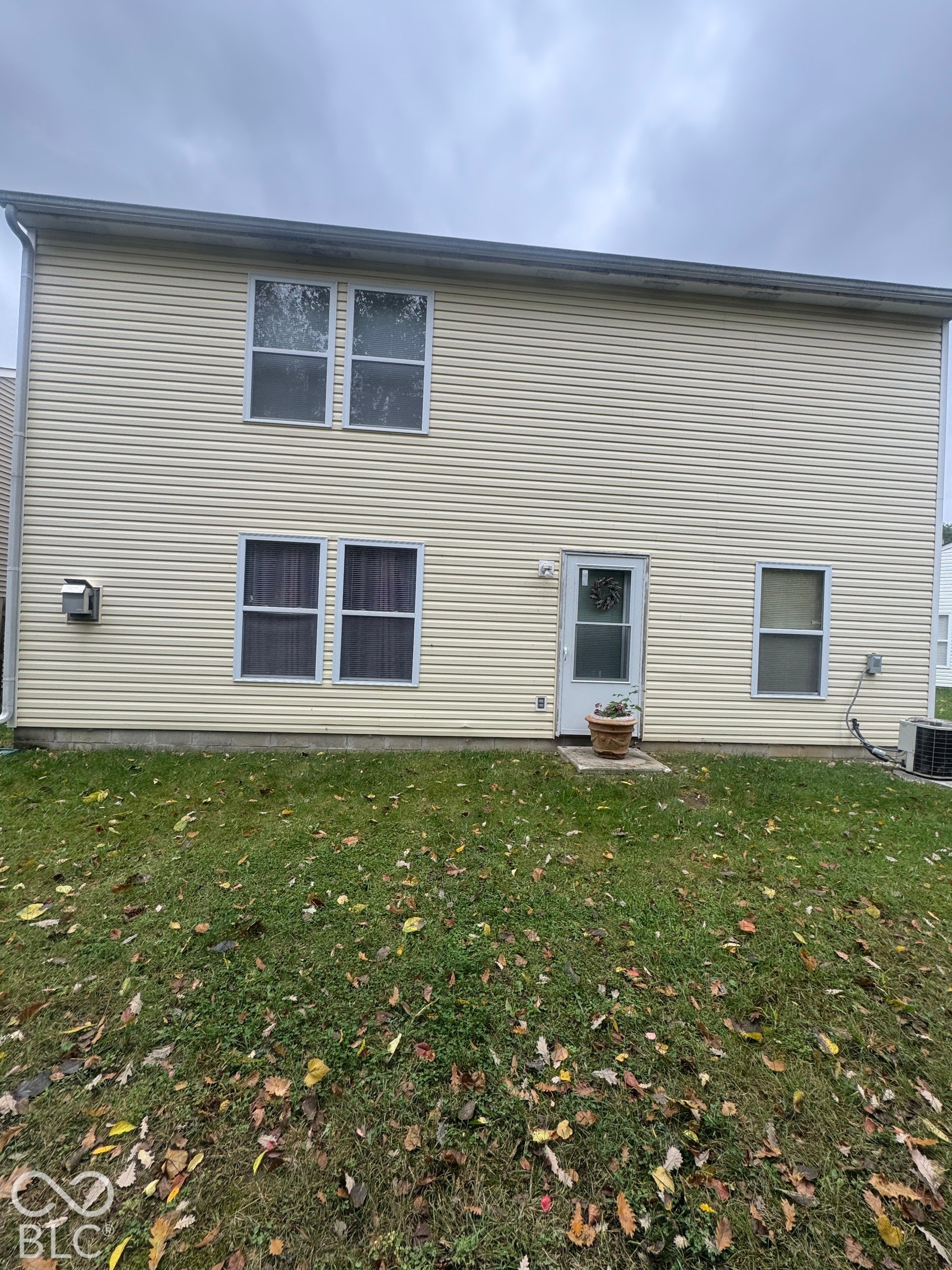 Two-story exterior featuring cream-colored vinyl siding, five double-hung windows, and a dedicated rear entry door with a concrete stoop