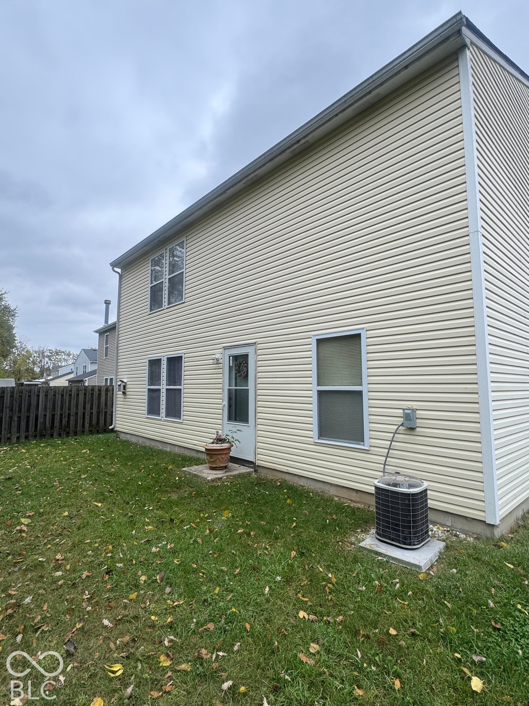 Two-story exterior featuring light-colored horizontal siding, multiple windows, a rear entry door, and a perimeter wood privacy fence