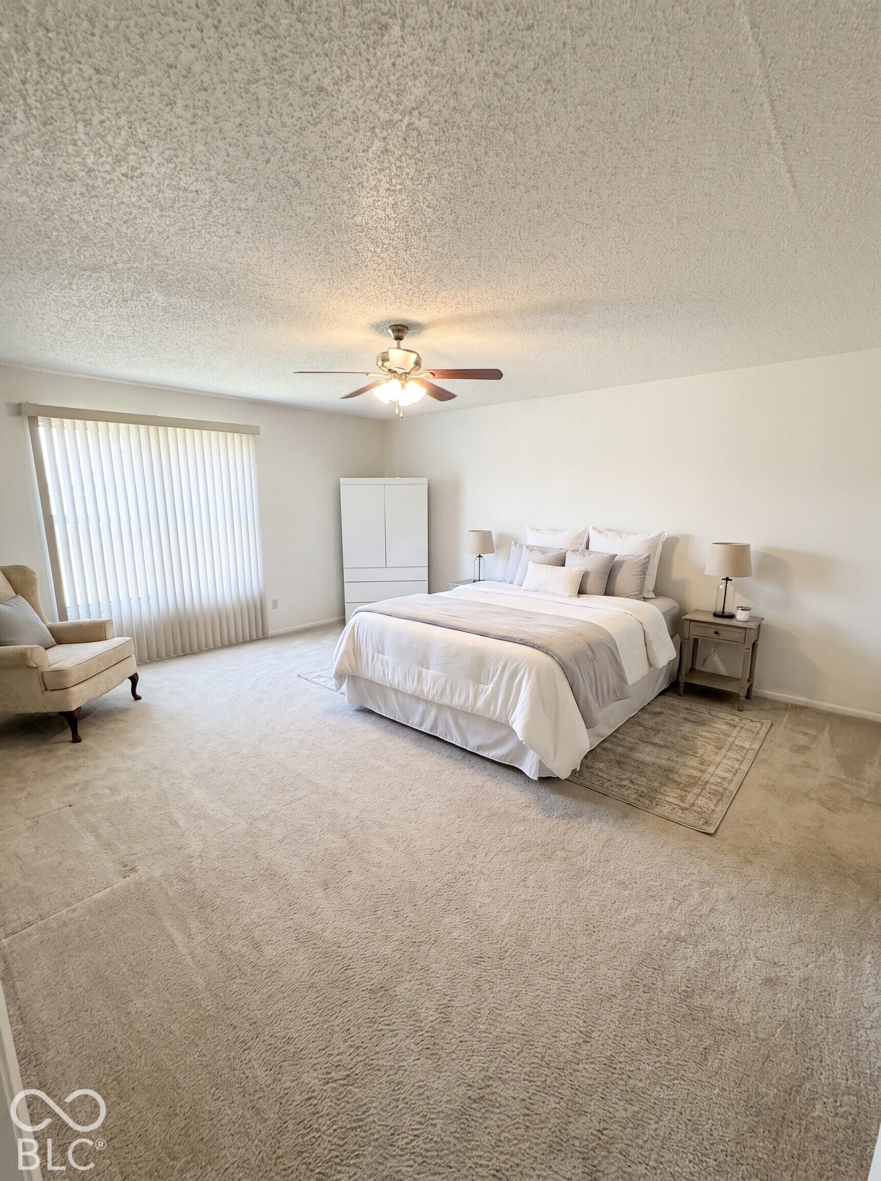 Virtually Altered - Spacious room featuring neutral carpeting, a textured ceiling, a ceiling fan with integrated lighting, and floor-to-ceiling vertical blinds