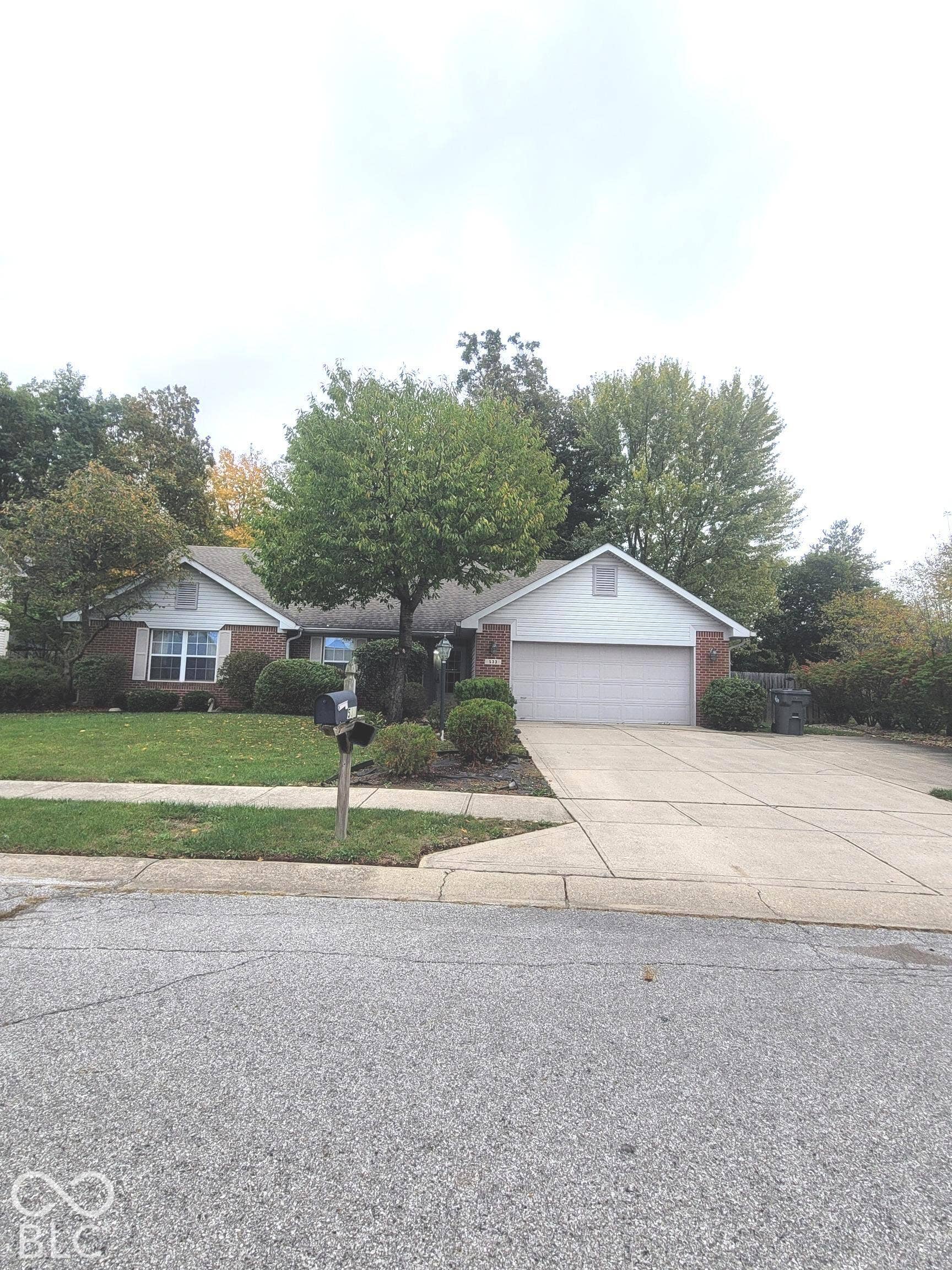 Single-story exterior featuring a brick and siding facade, attached two-car garage, concrete driveway extended to accommodate additional parking, and lush landscaping