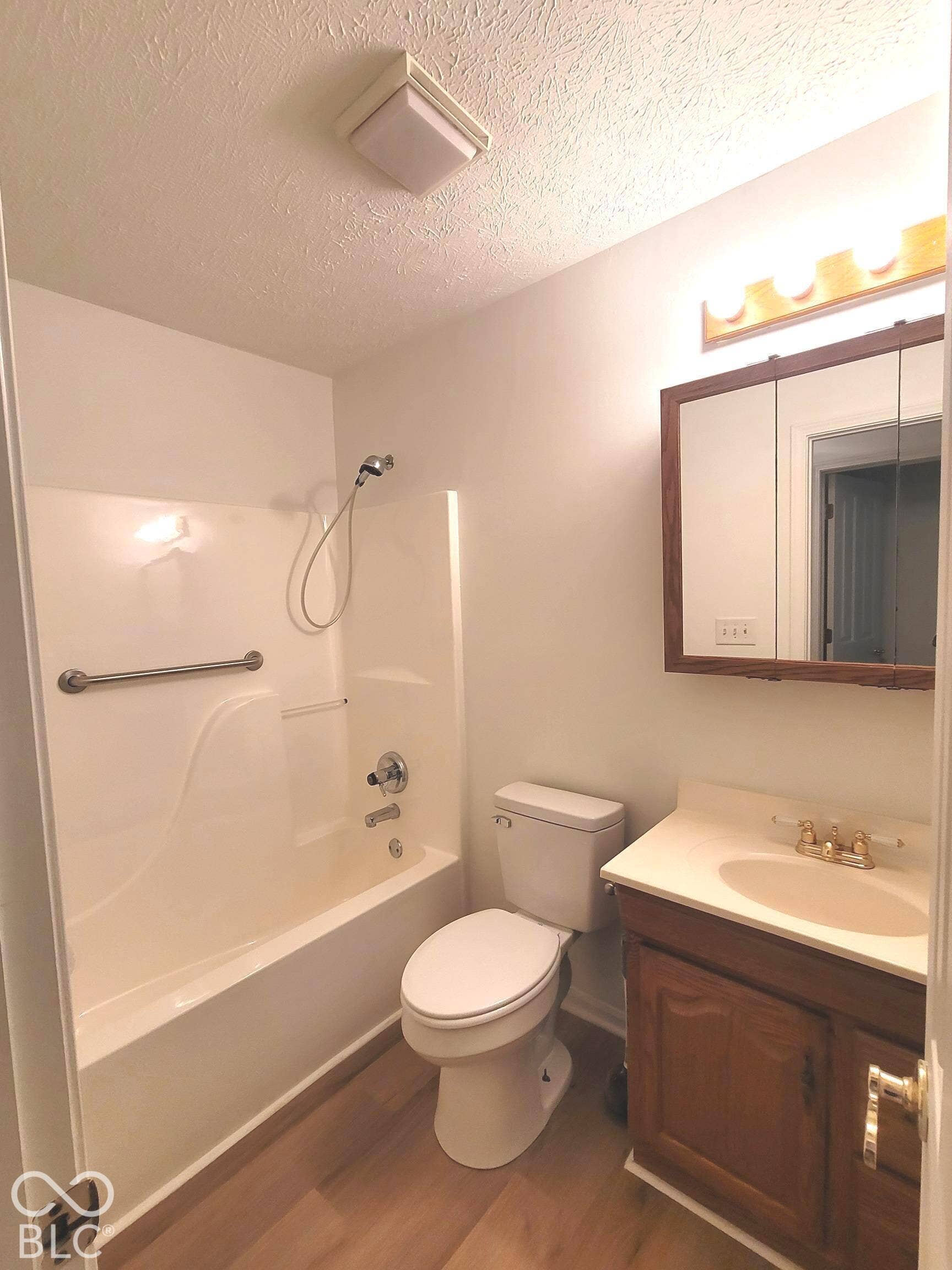Virtually Altered - Bathroom featuring a bathtub and shower combination, a wood-finish vanity cabinet, a tri-fold medicine cabinet, and wood-finish flooring
