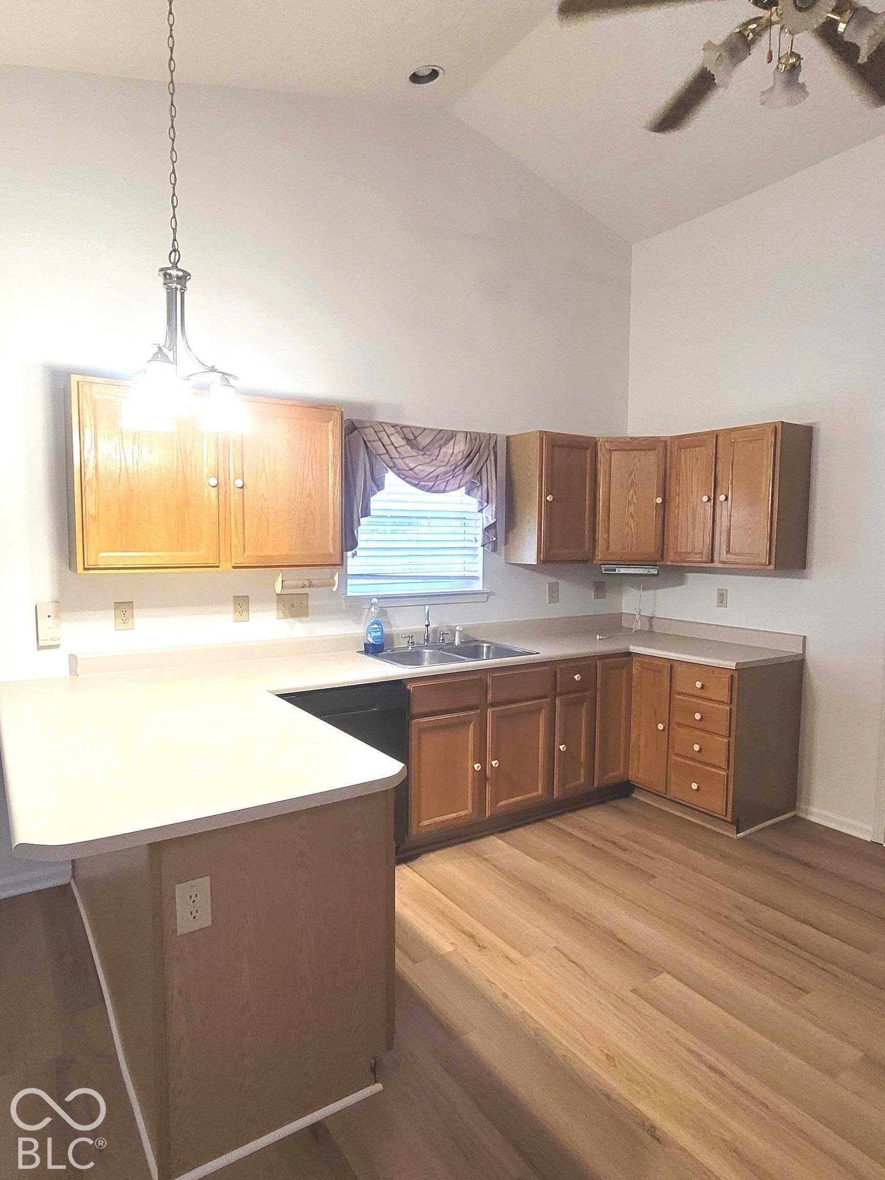 Kitchen featuring wood cabinetry, solid surface countertops, dual-basin stainless steel sink, wood-finish flooring, and vaulted ceiling