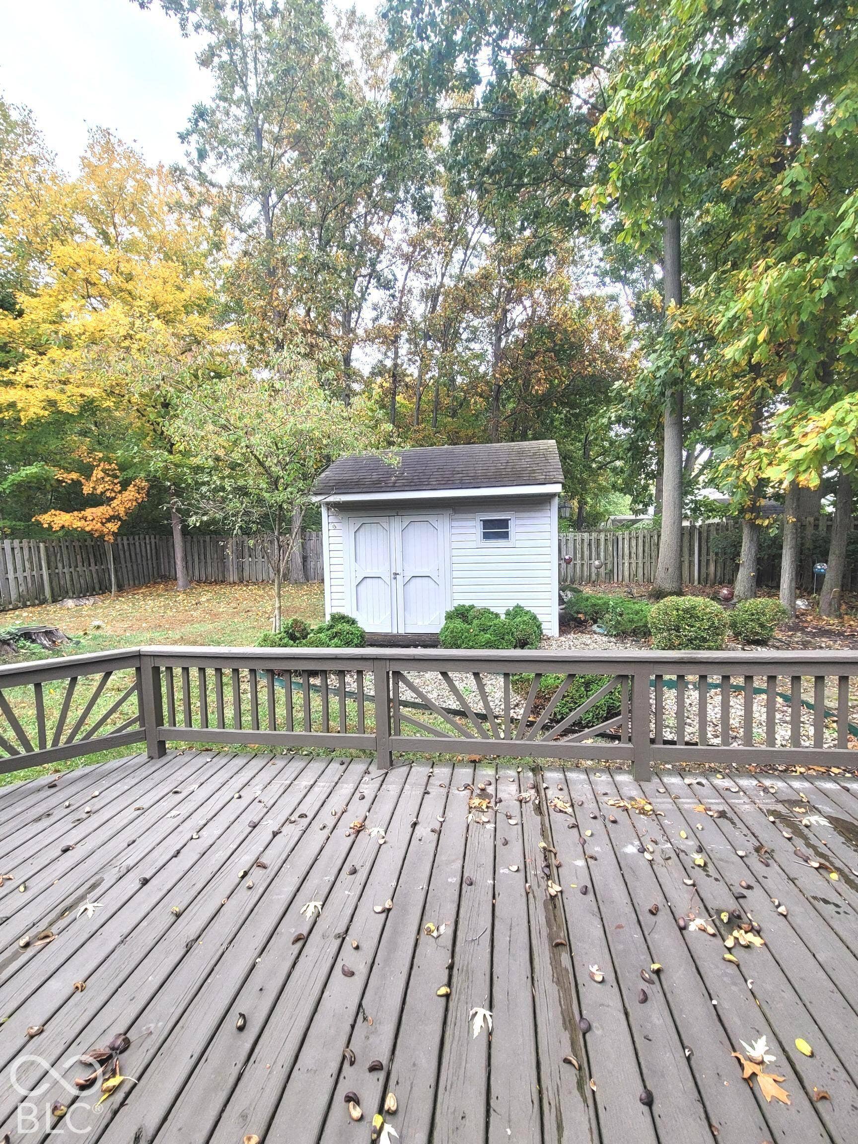 Elevated wood deck featuring decorative sunburst railings, detached storage shed with double doors, and private fenced-in backyard