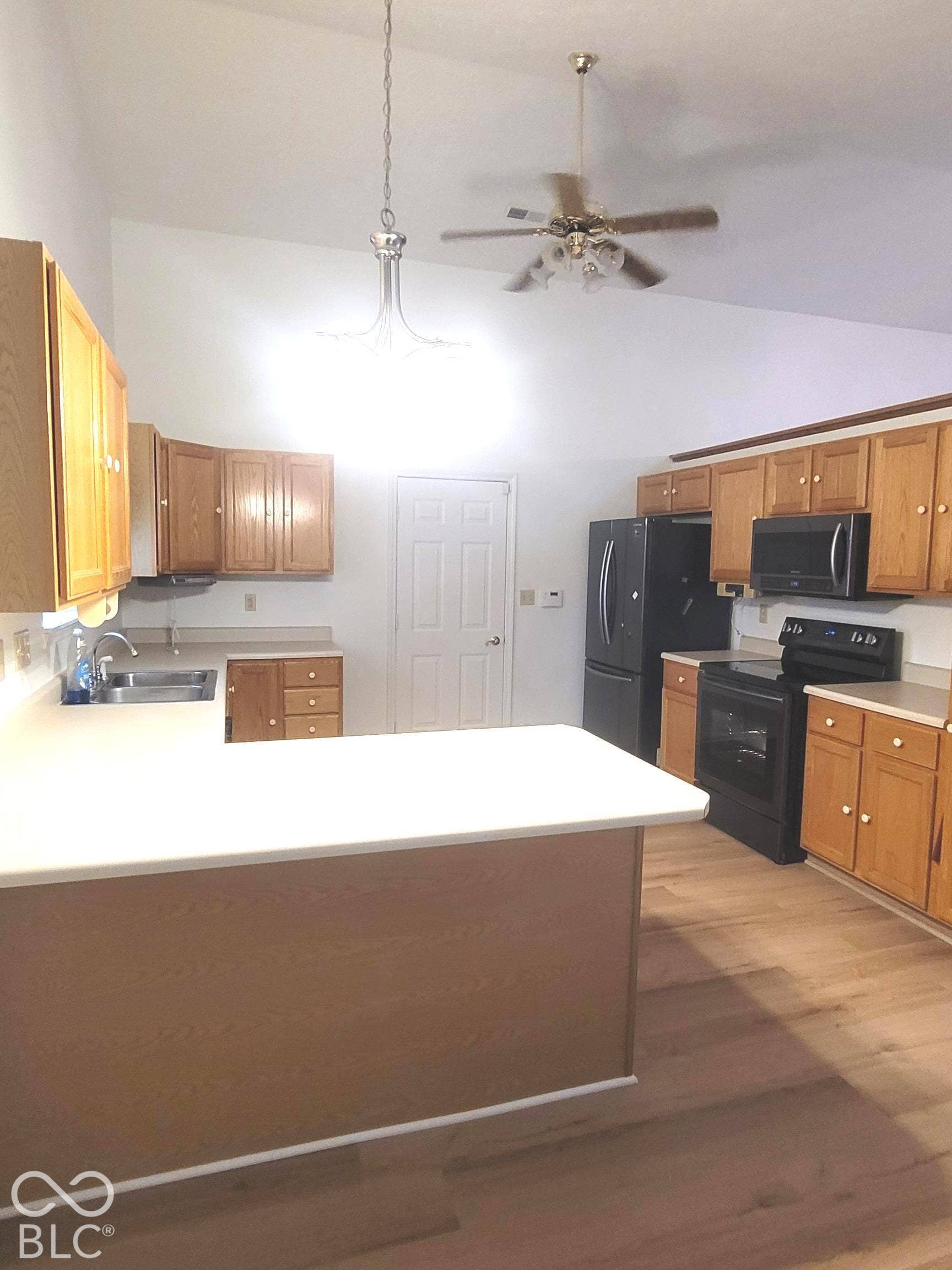 Kitchen featuring wood cabinetry, a peninsula with a solid-surface countertop, vaulted ceilings, and wood-finish flooring