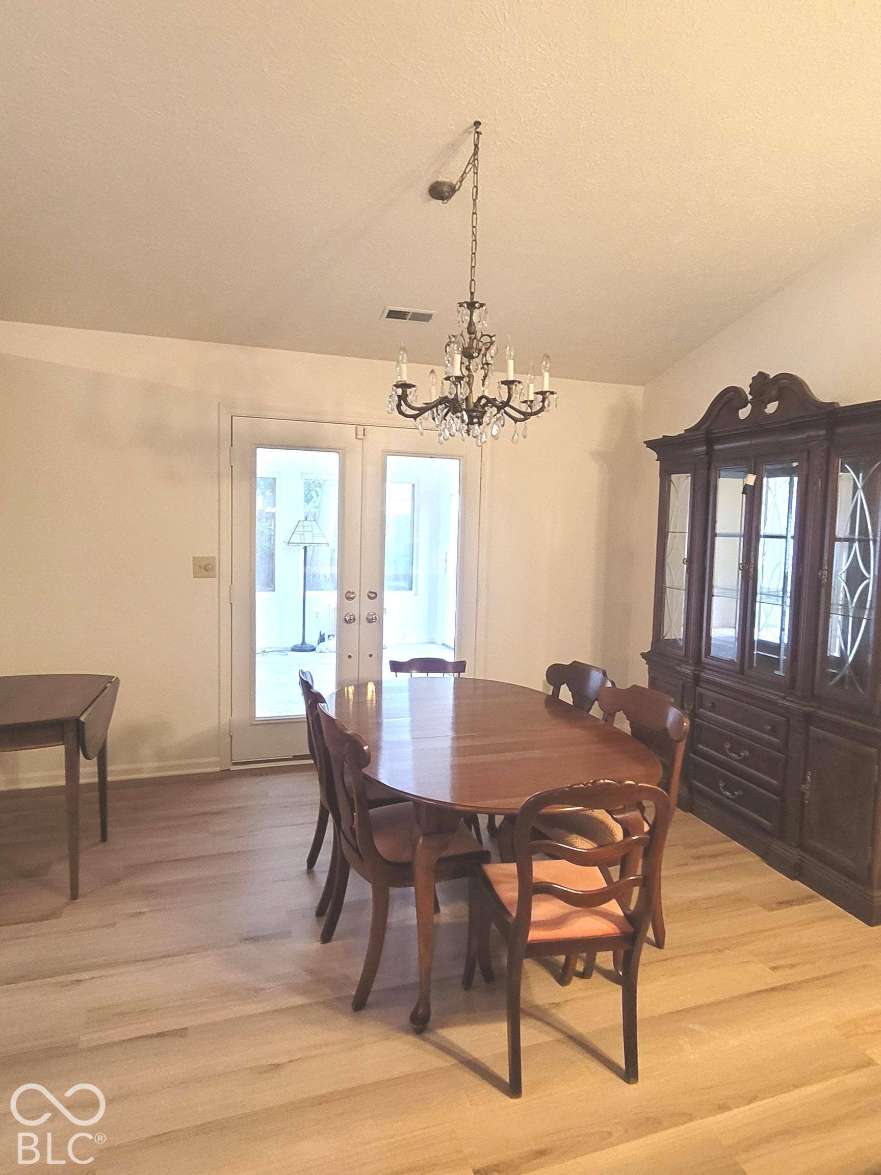 Wood-finish flooring, vaulted ceilings, and glass-paneled French doors leading to an enclosed porch, accented by a decorative tiered chandelier