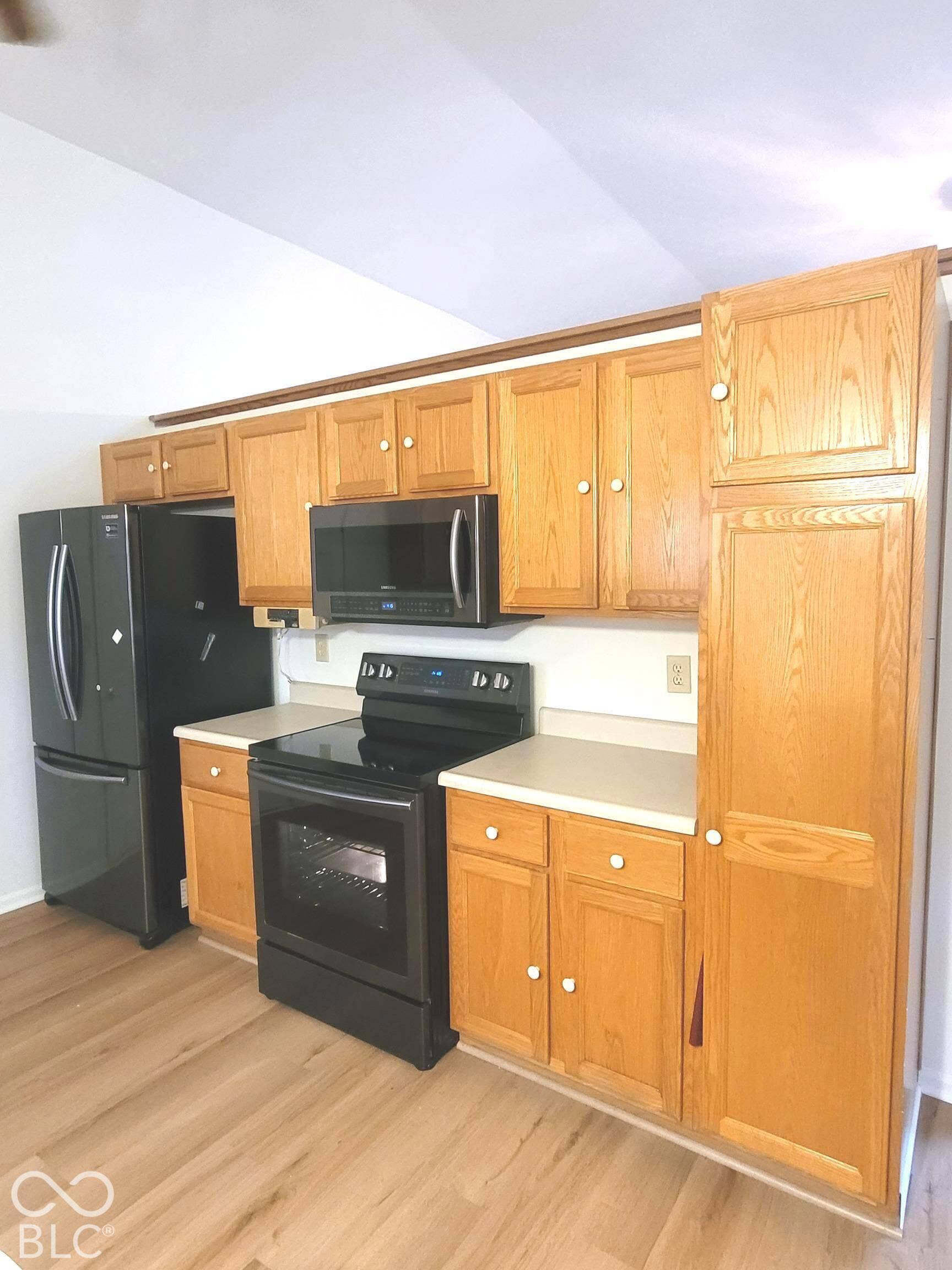 Kitchen featuring oak cabinetry, light-toned solid surface countertops, wood-finish flooring, and black appliances including a built-in microwave and range
