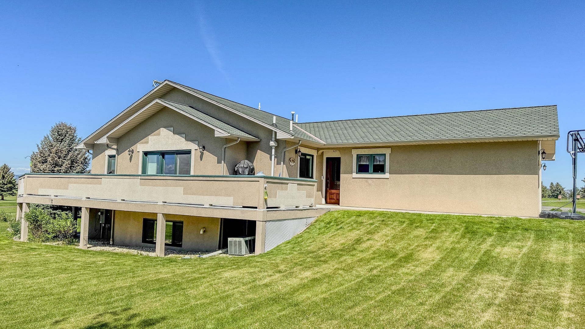 4134 Fox Ridge Drive, Helena, MT 59602 Back of property featuring stucco siding, a lawn, central AC unit, and a wooden deck