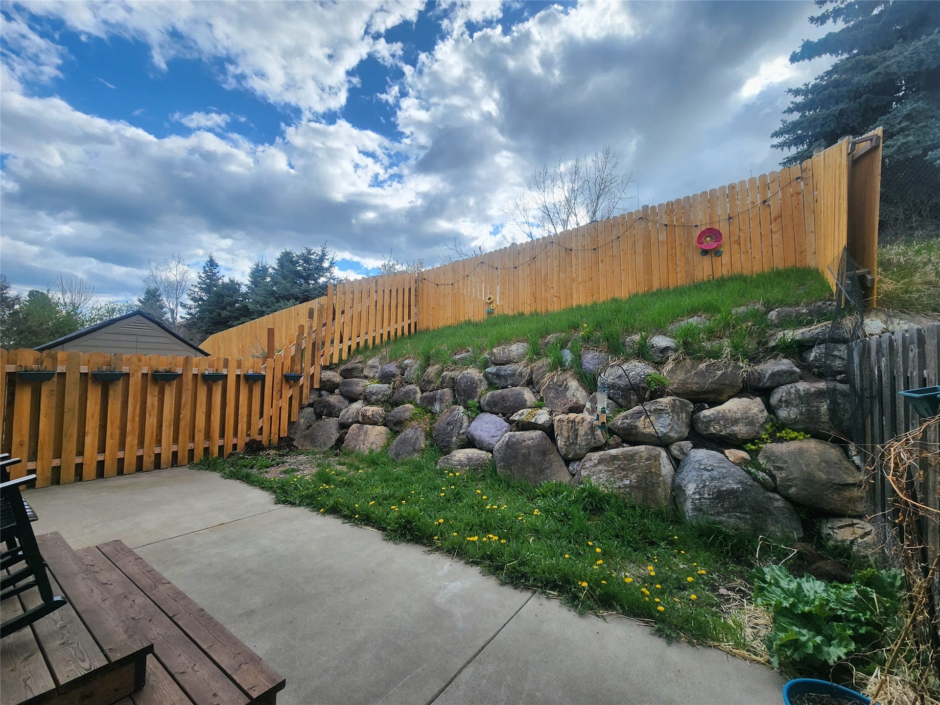 114 Sunrise Terrace, #114, Bigfork, MT 59911 Concrete patio with wood-finish decking, surrounded by a wood privacy fence and a natural stone retaining wall