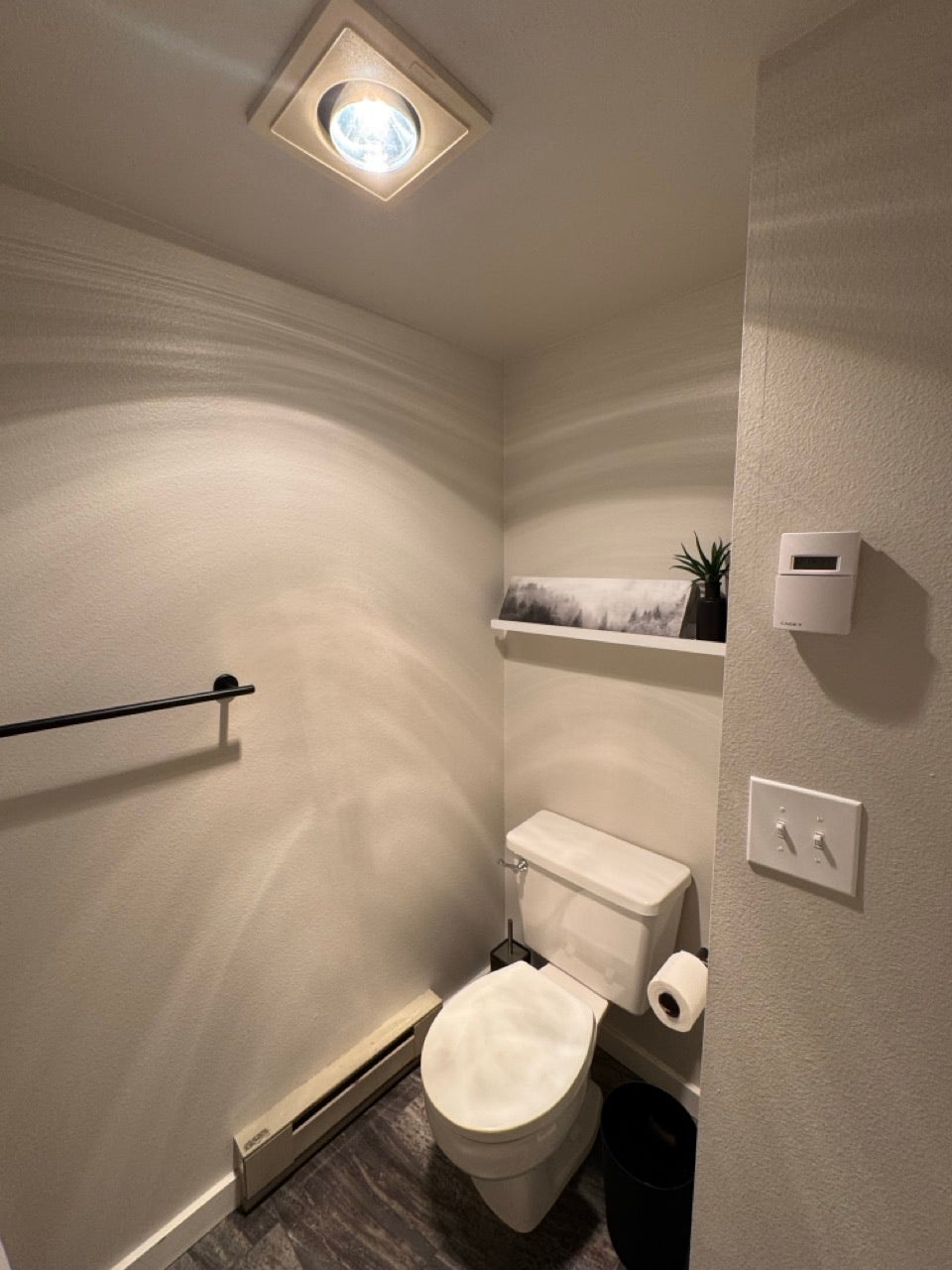 Compact powder room featuring a white toilet, wood-finish flooring, and a towel bar