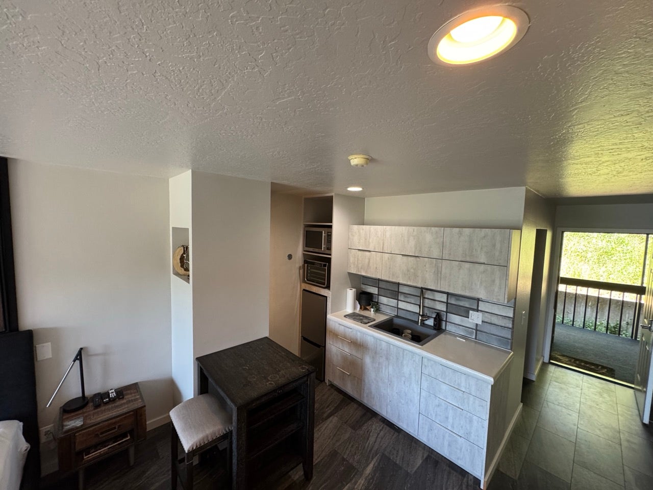 Compact kitchen featuring wood-finish cabinetry, solid surface countertops, and a tiled backsplash