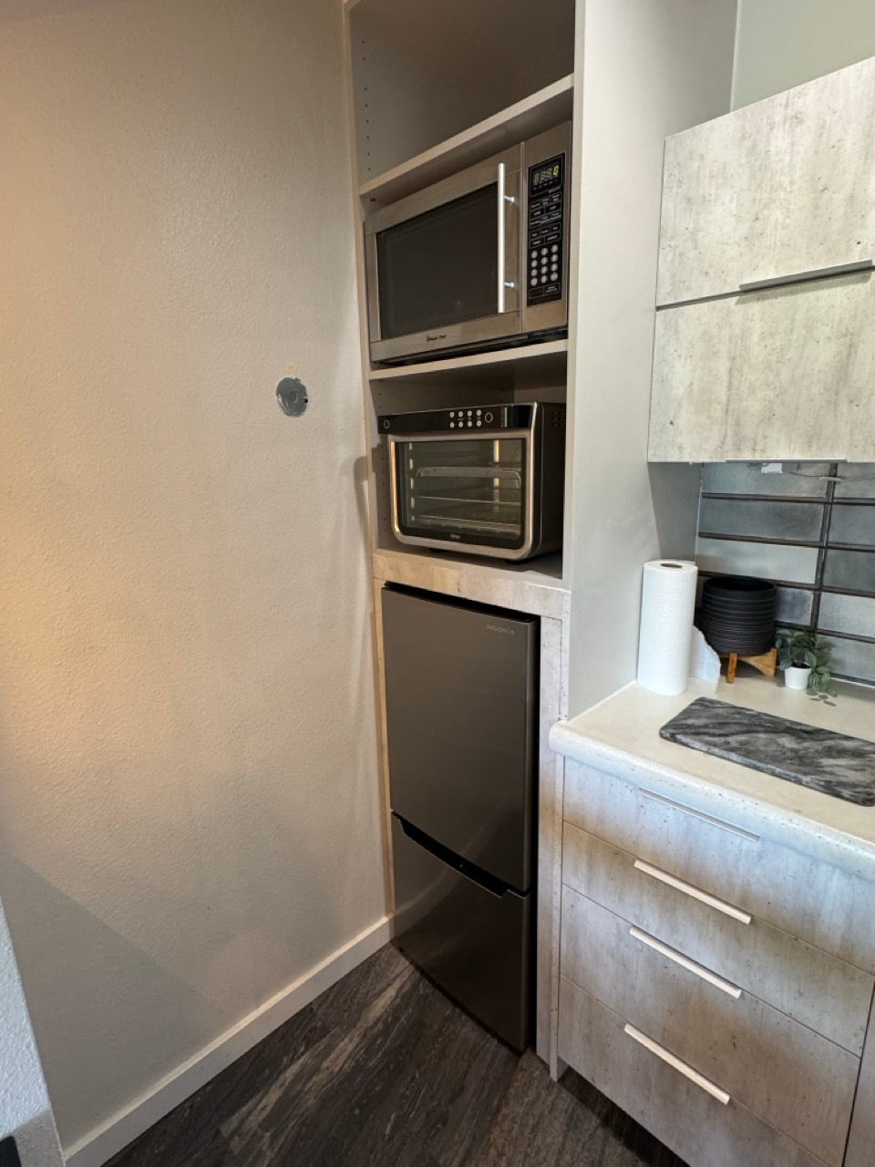 Integrated kitchen appliances featuring a built-in microwave, compact refrigerator, and a countertop with textured cabinetry and modern hardware