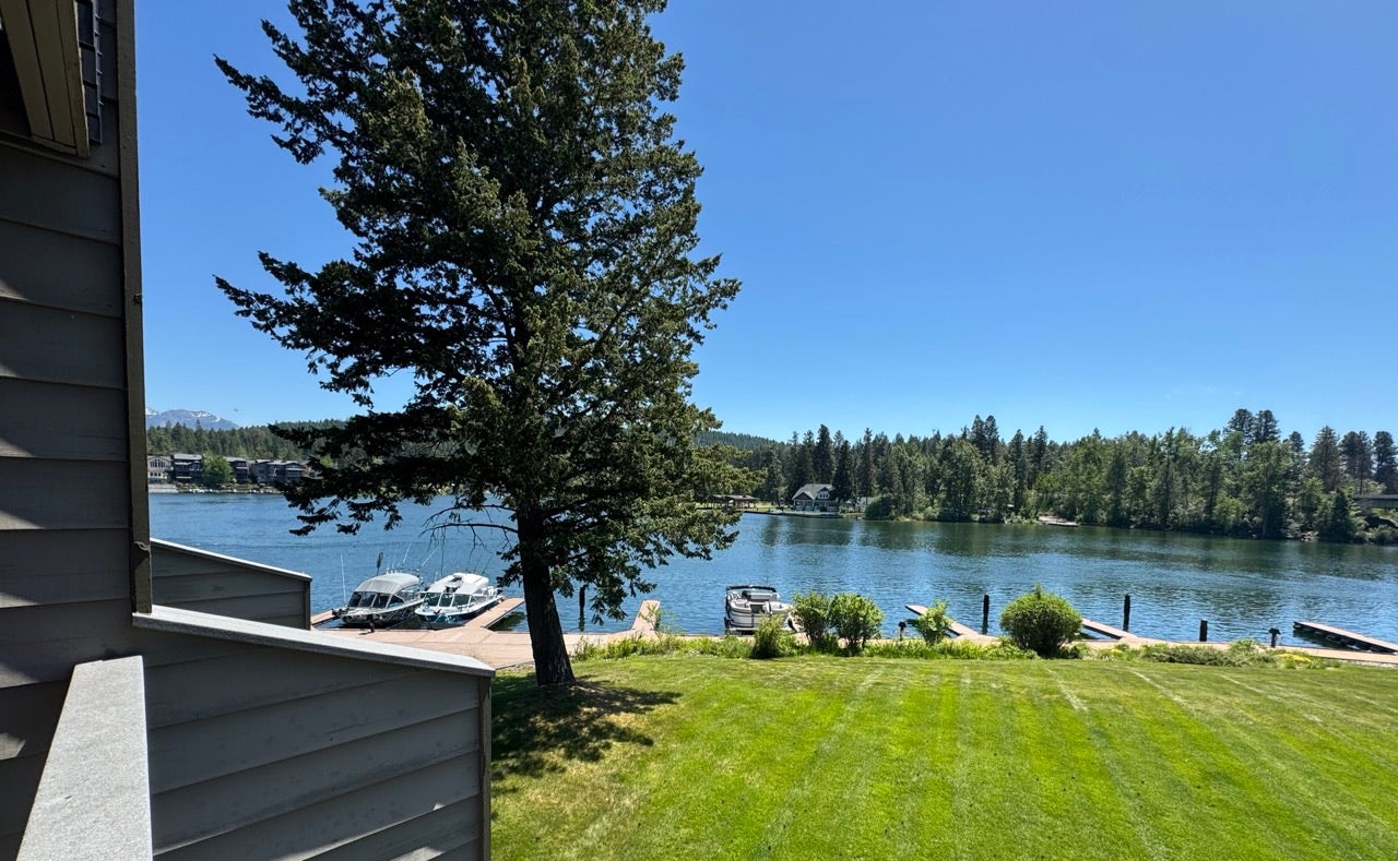 Expansive waterfront setting featuring a grassy lawn, mature trees, and a private dock